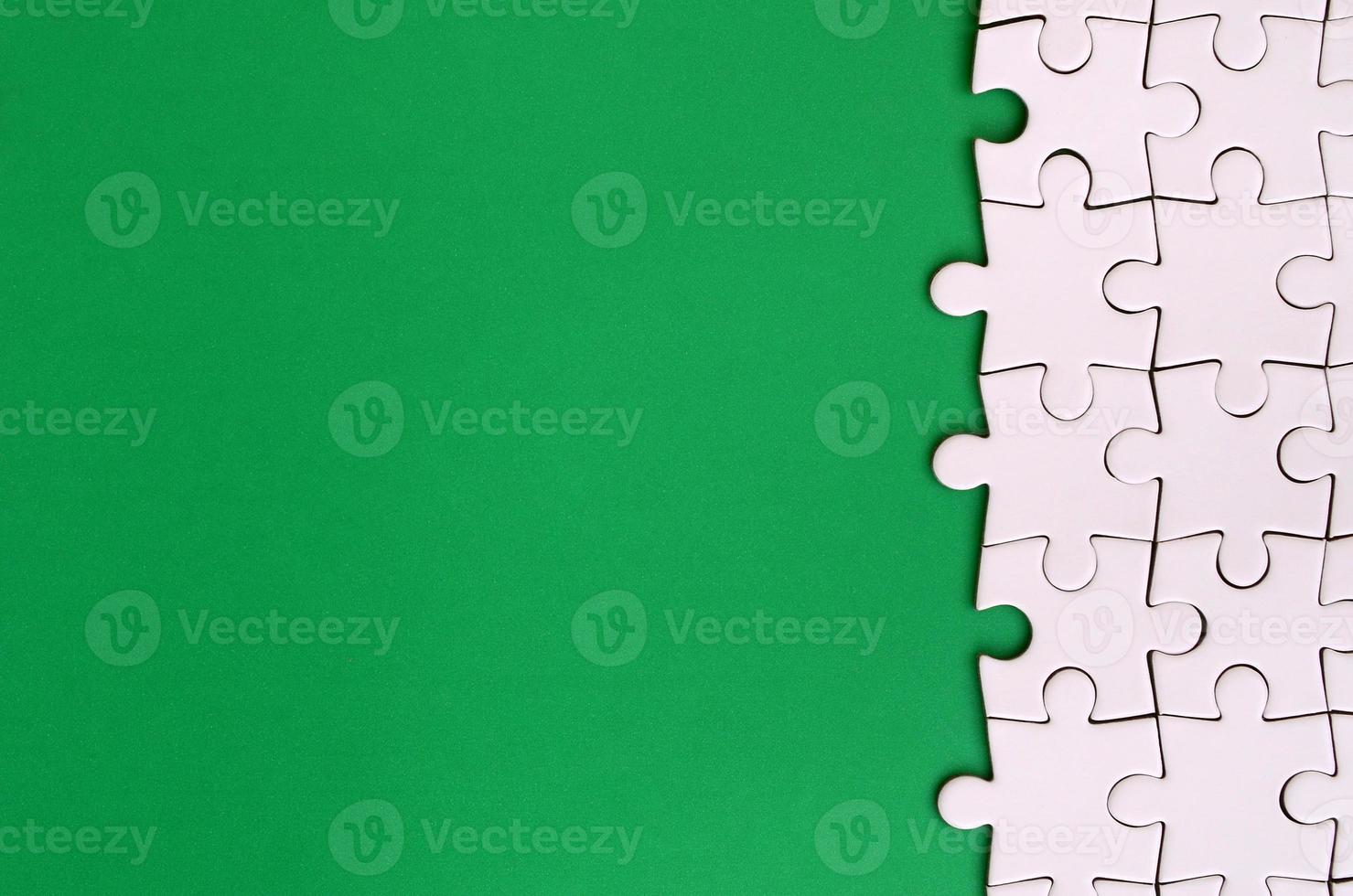 Fragment of a folded white jigsaw puzzle on the background of a green plastic surface. Texture photo with copy space for text