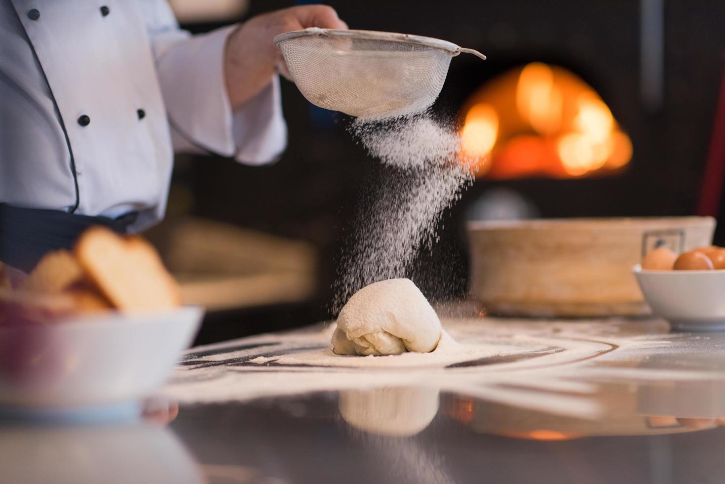 chef sprinkling flour over fresh pizza dough photo