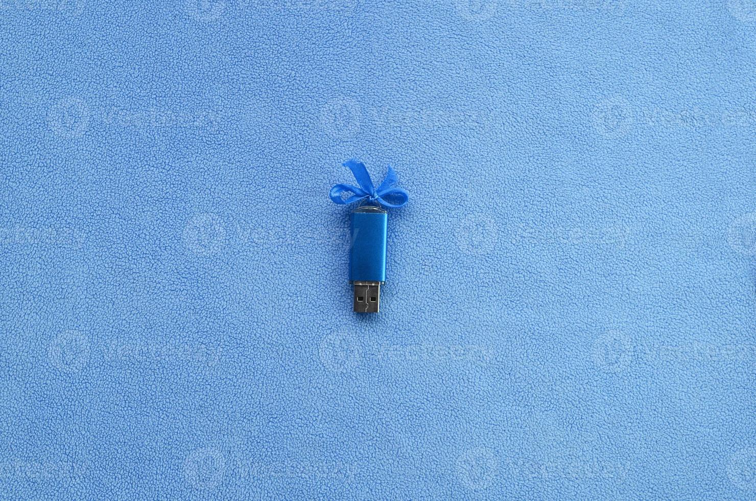 Brilliant blue usb flash memory card with a blue bow lies on a blanket of soft and furry light blue fleece fabric. Classic female gift design for a memory card photo