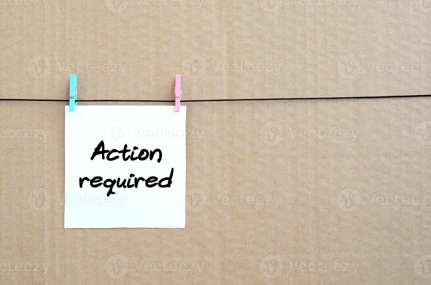 Action required Note is written on a white sticker that hangs with a clothespin on a rope on a background of brown cardboard photo