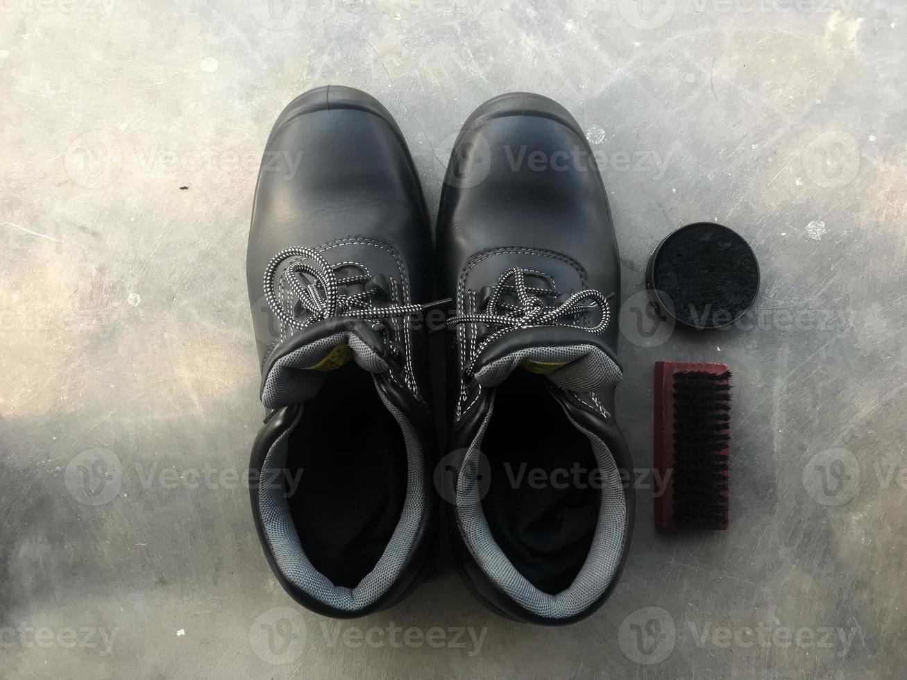 zapatos de seguridad negros junto a un cepillo para zapatos y betún para zapatos foto