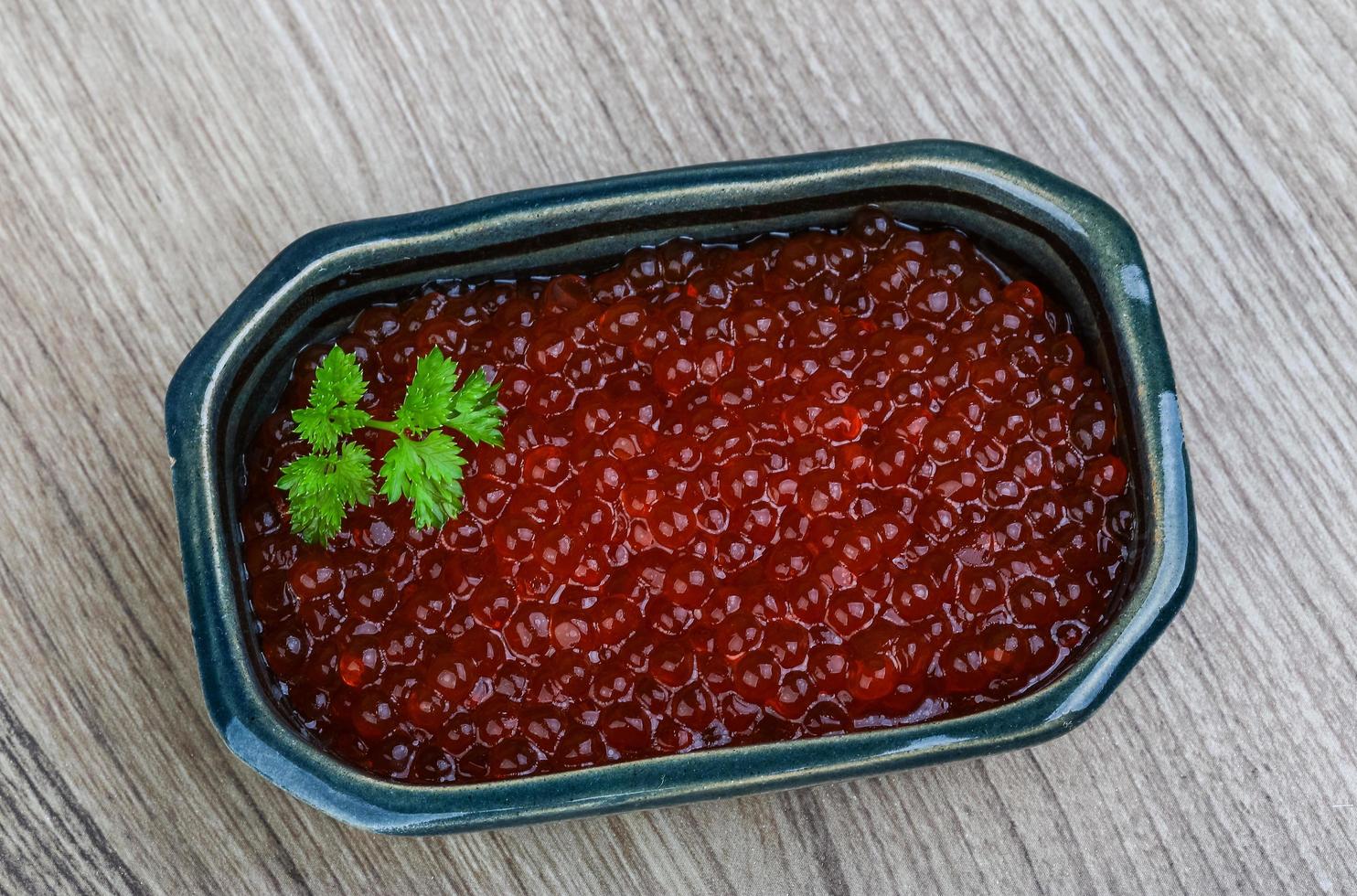 caviar rojo en un recipiente sobre fondo de madera foto