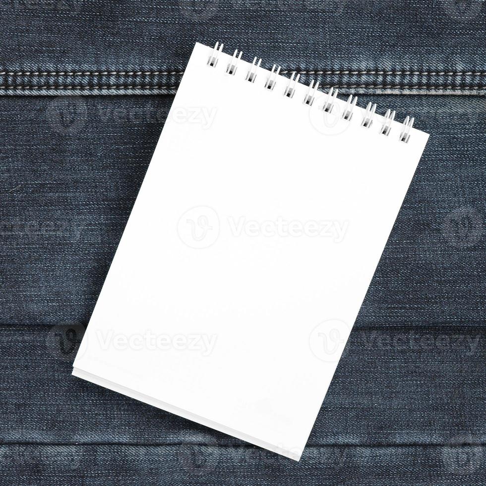 White notebook with clean pages lying on dark blue jeans background. Image with copy space photo