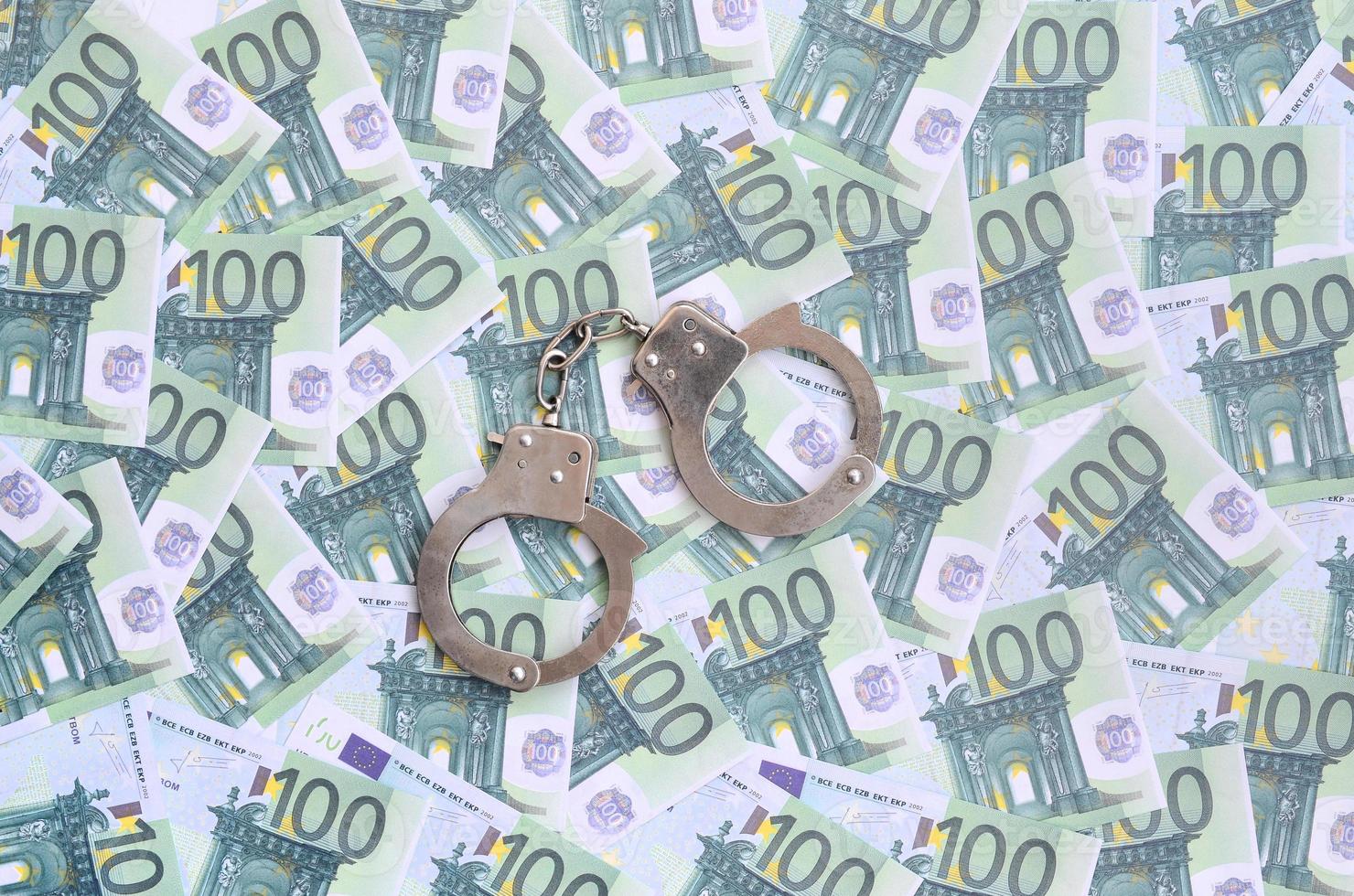 Police handcuffs lies on a set of green monetary denominations of 100 euros. A lot of money forms an infinite heap photo