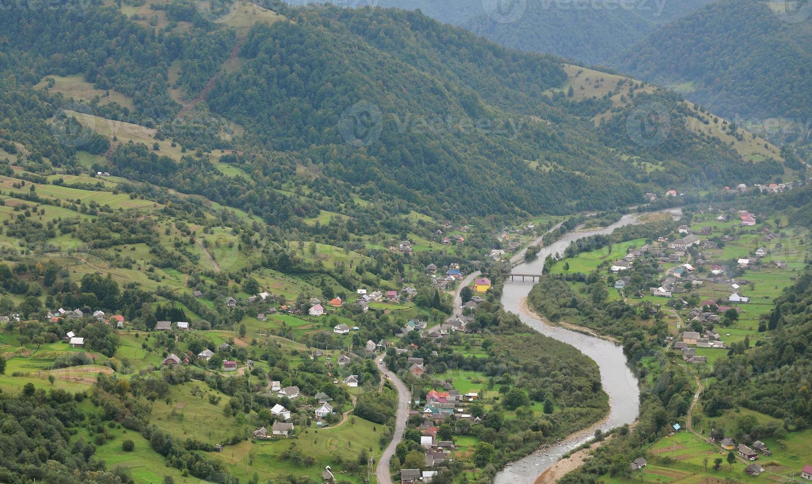 A beautiful view of the village of Mezhgorye, Carpathian region. A lot of residential buildings surrounded by high forest mountains and long river photo