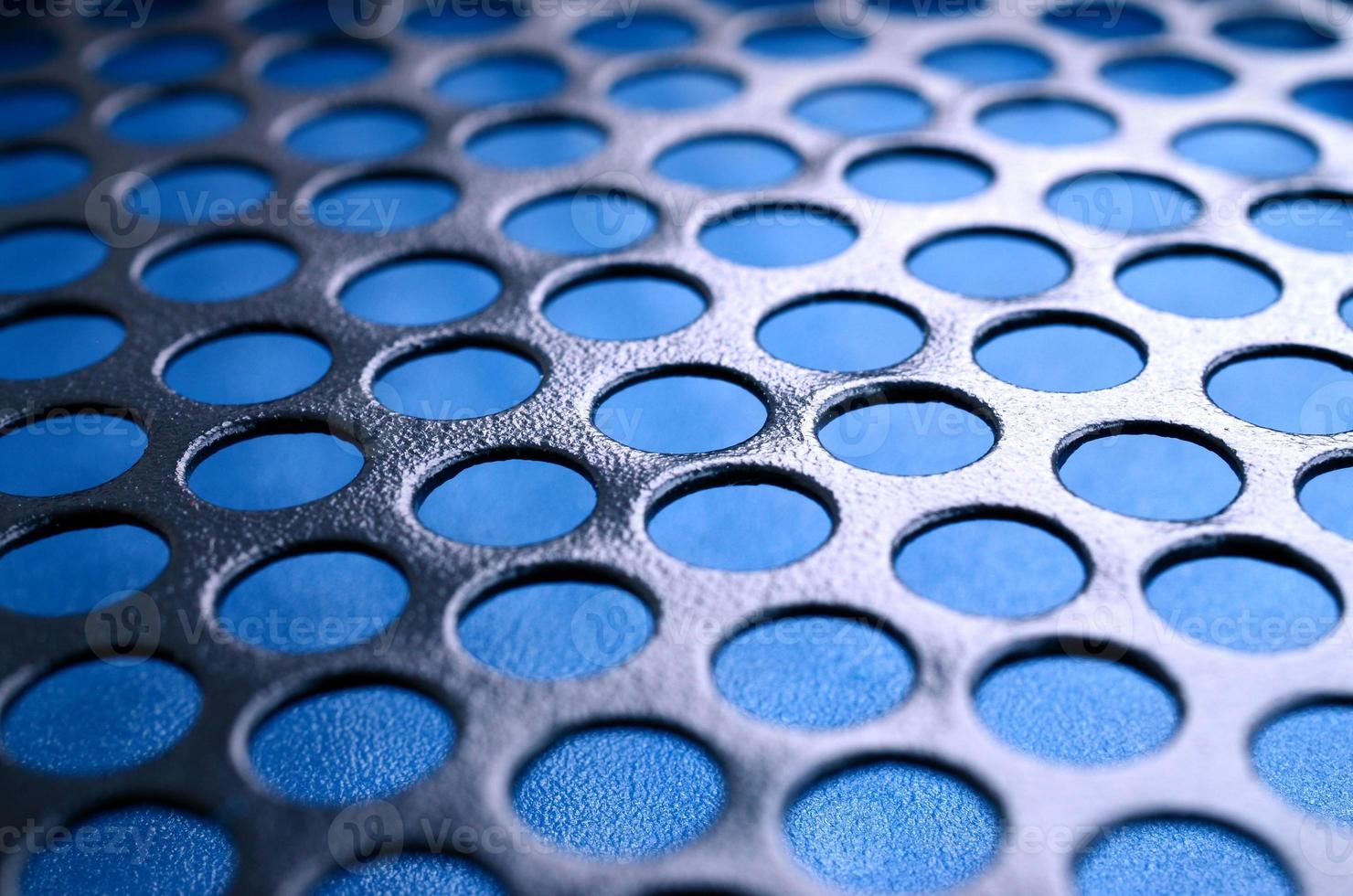 Black metal computer case panel mesh with holes on blue background. Abstract close up image photo