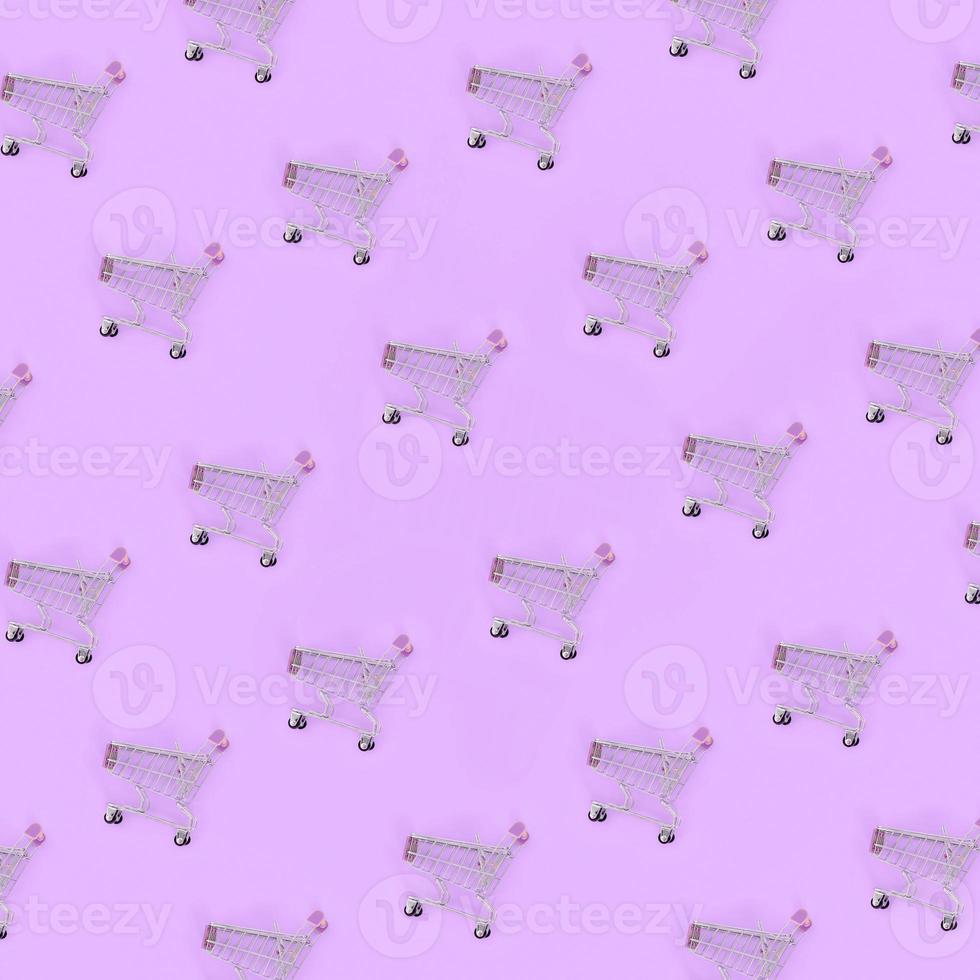 Shopping addiction, shopping lover or shopaholic concept. Many small empty shopping carts perform a pattern on a pastel colored paper background. Flat lay composition, top view photo