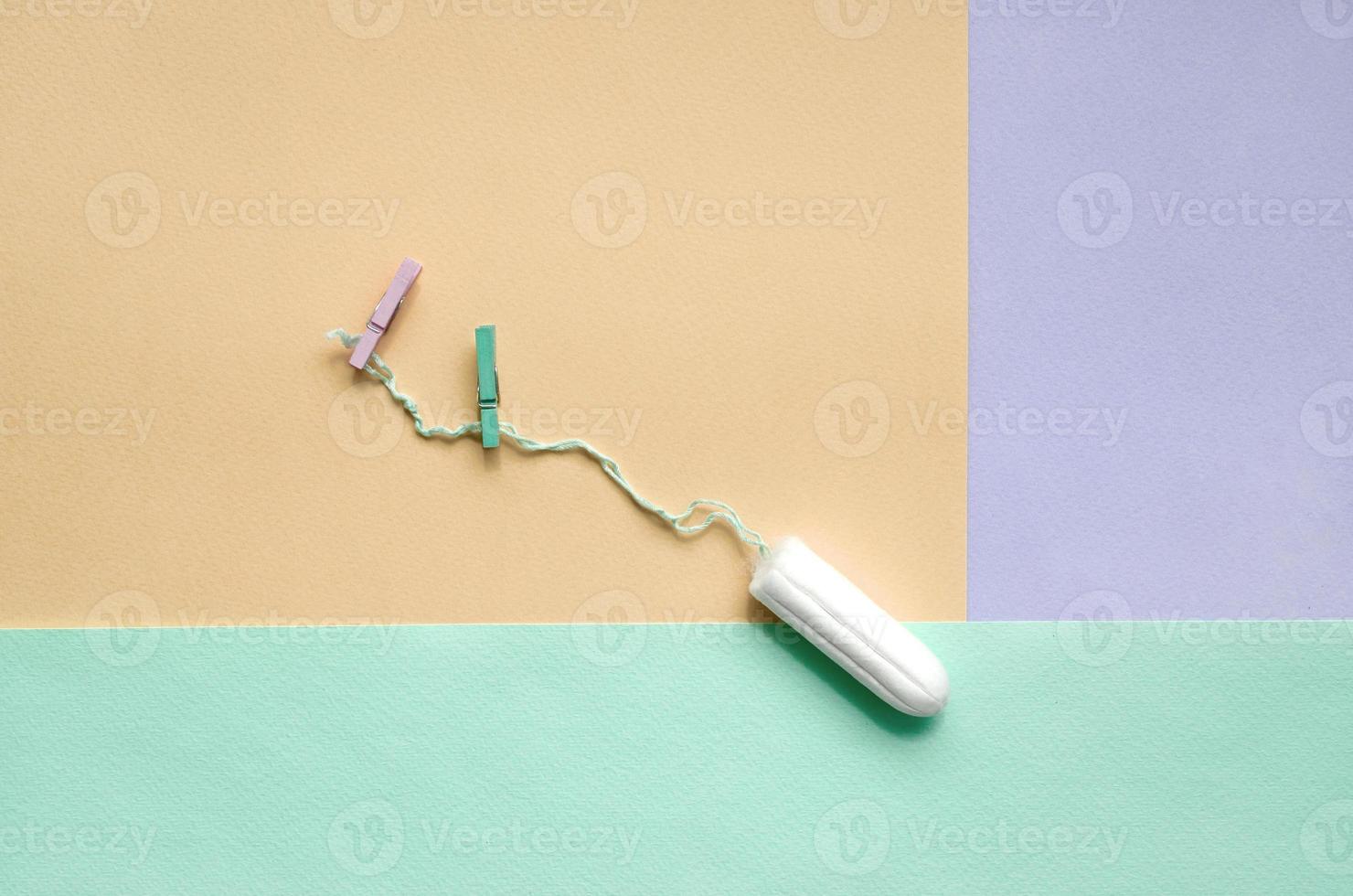 Tampon with two clothespins lie on texture background of fashion pastel violet, yellow and blue colors photo