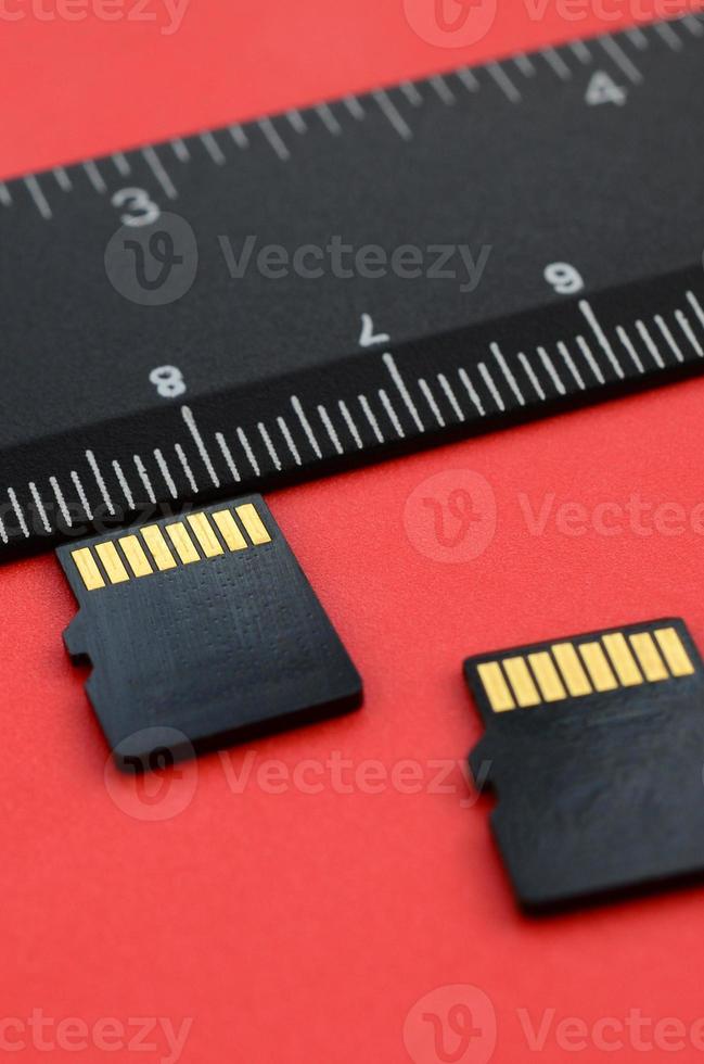 Two small micro SD memory cards lie on a red background next to a black ruler. A small and compact data and information store photo
