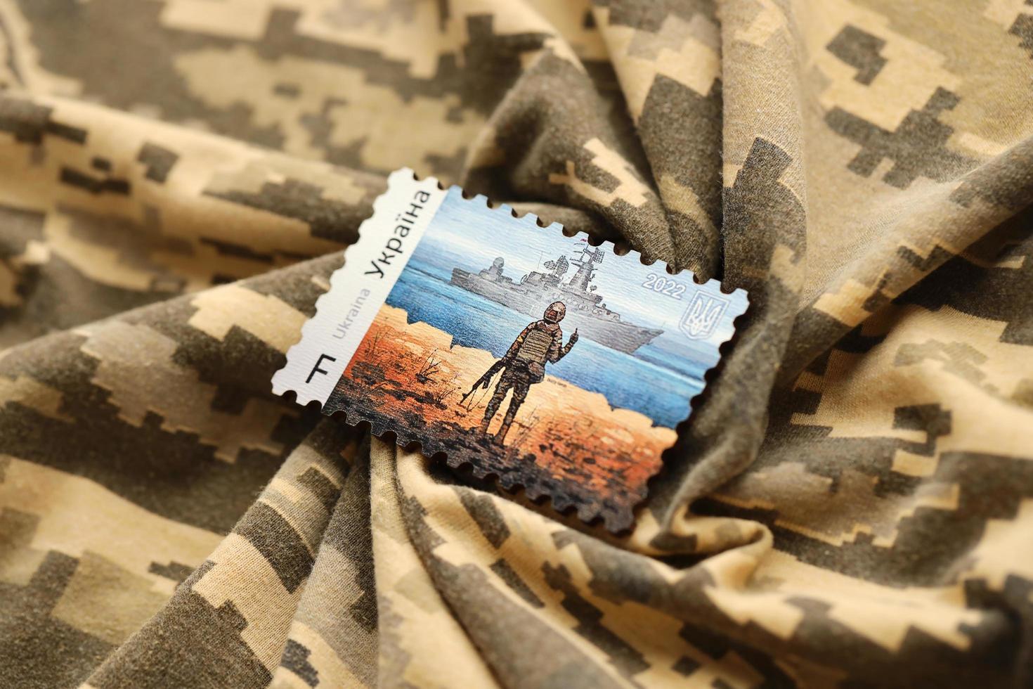 TERNOPIL, UKRAINE - SEPTEMBER 2, 2022 Famous Ukrainian postmark with russian warship and ukrainian soldier as wooden souvenir on army camouflage uniform photo