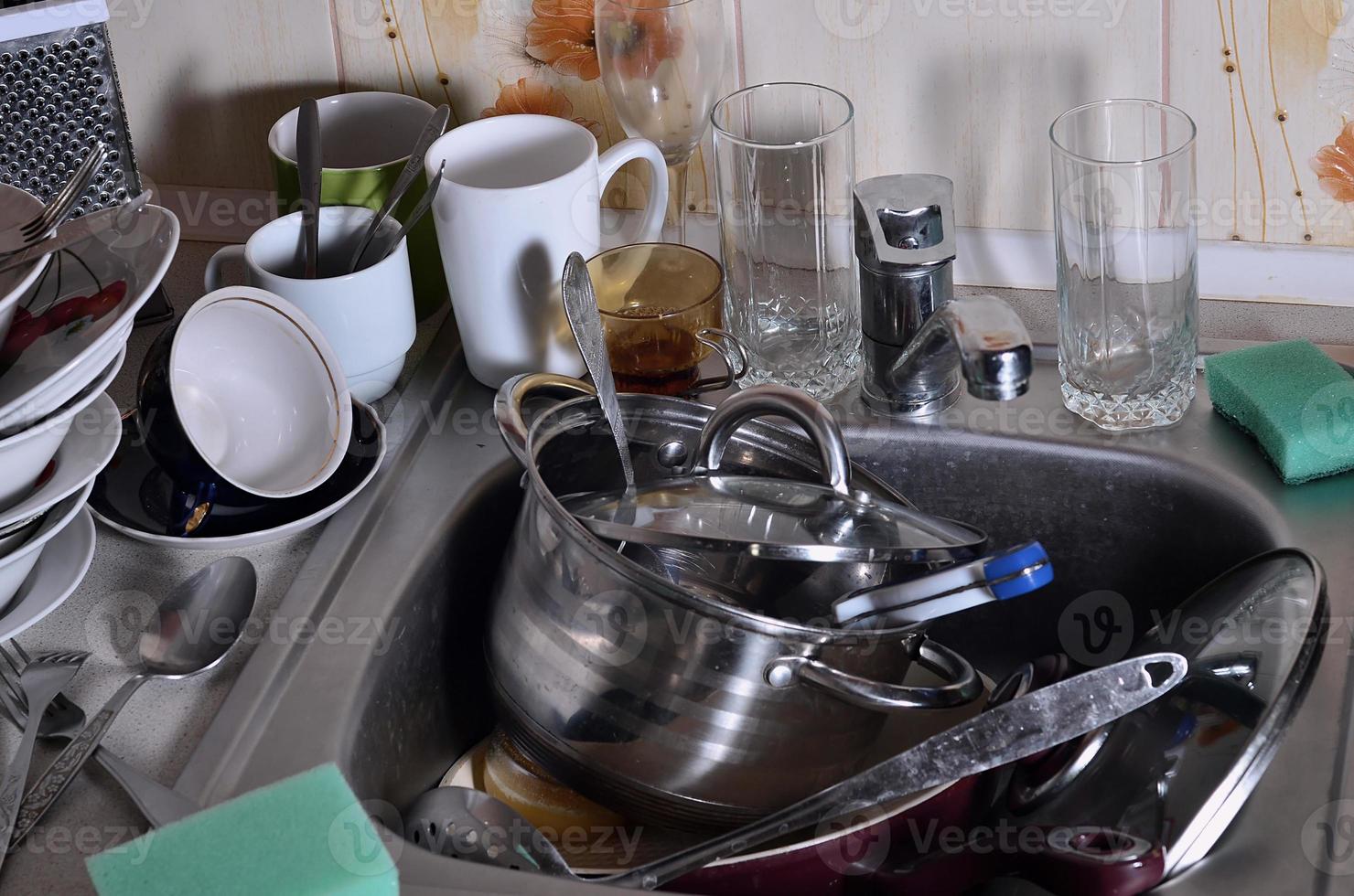 una enorme pila de platos sin lavar en el fregadero de la cocina y en la encimera foto