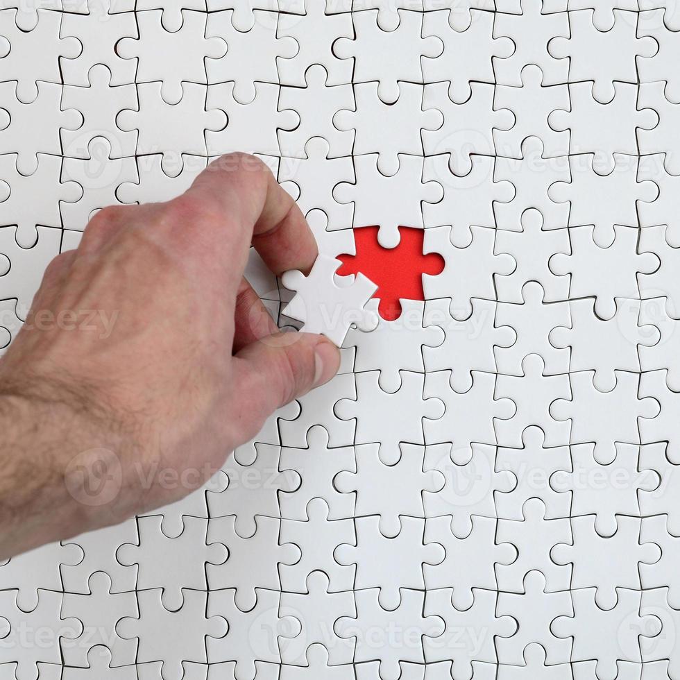 The texture of a white puzzle puzzle in the assembled state with one missing element that the male hand puts in photo