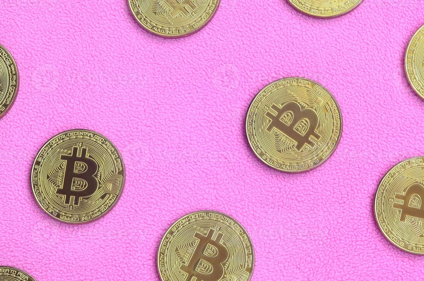 Many golden bitcoins lies on a blanket made of soft and fluffy light pink fleece fabric. Physical visualization of virtual crypto currency photo