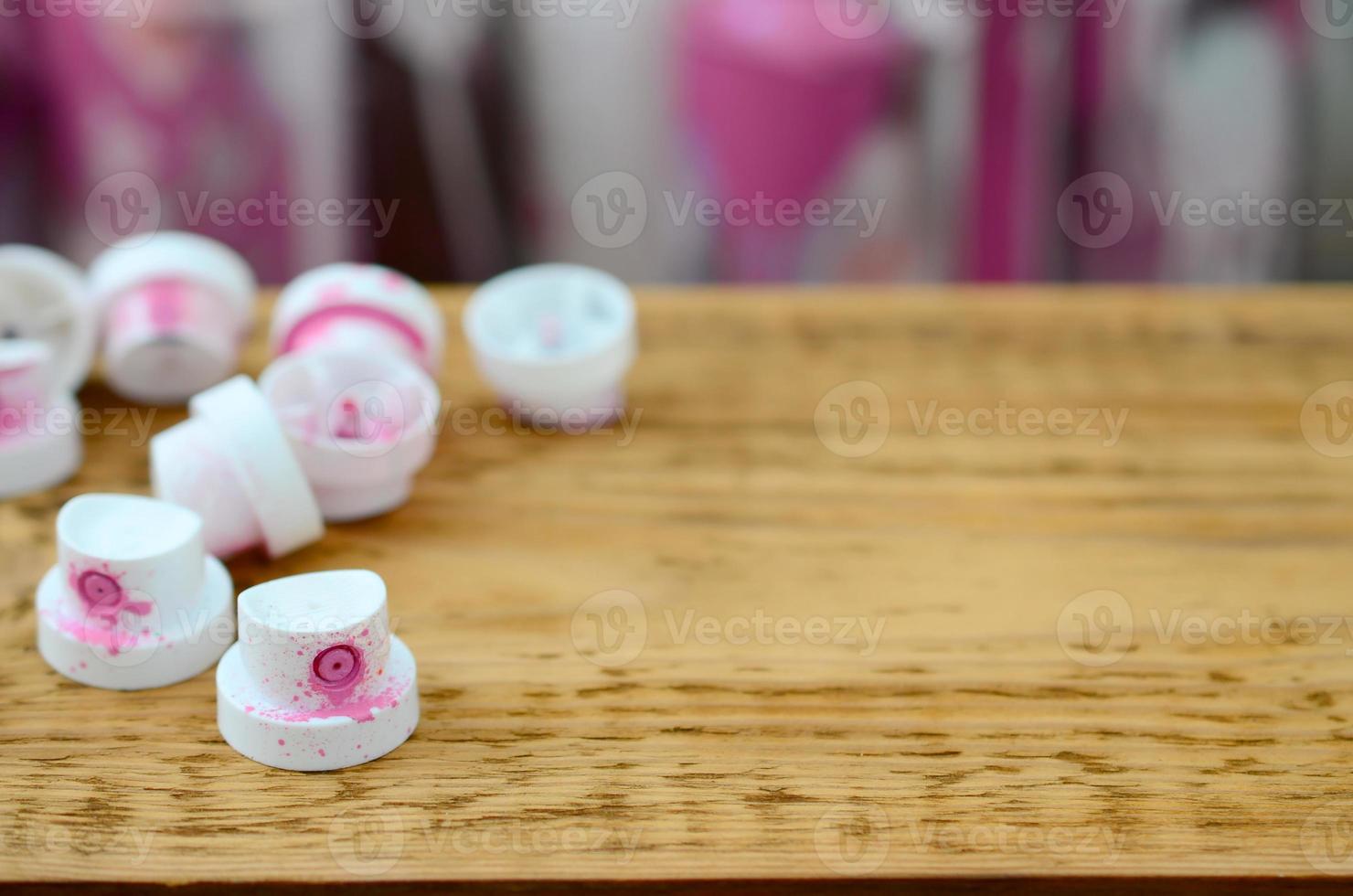 The soiled pink nozzles from the paint sprayer lies on a wooden plank on a background of a many dirty spray cans photo