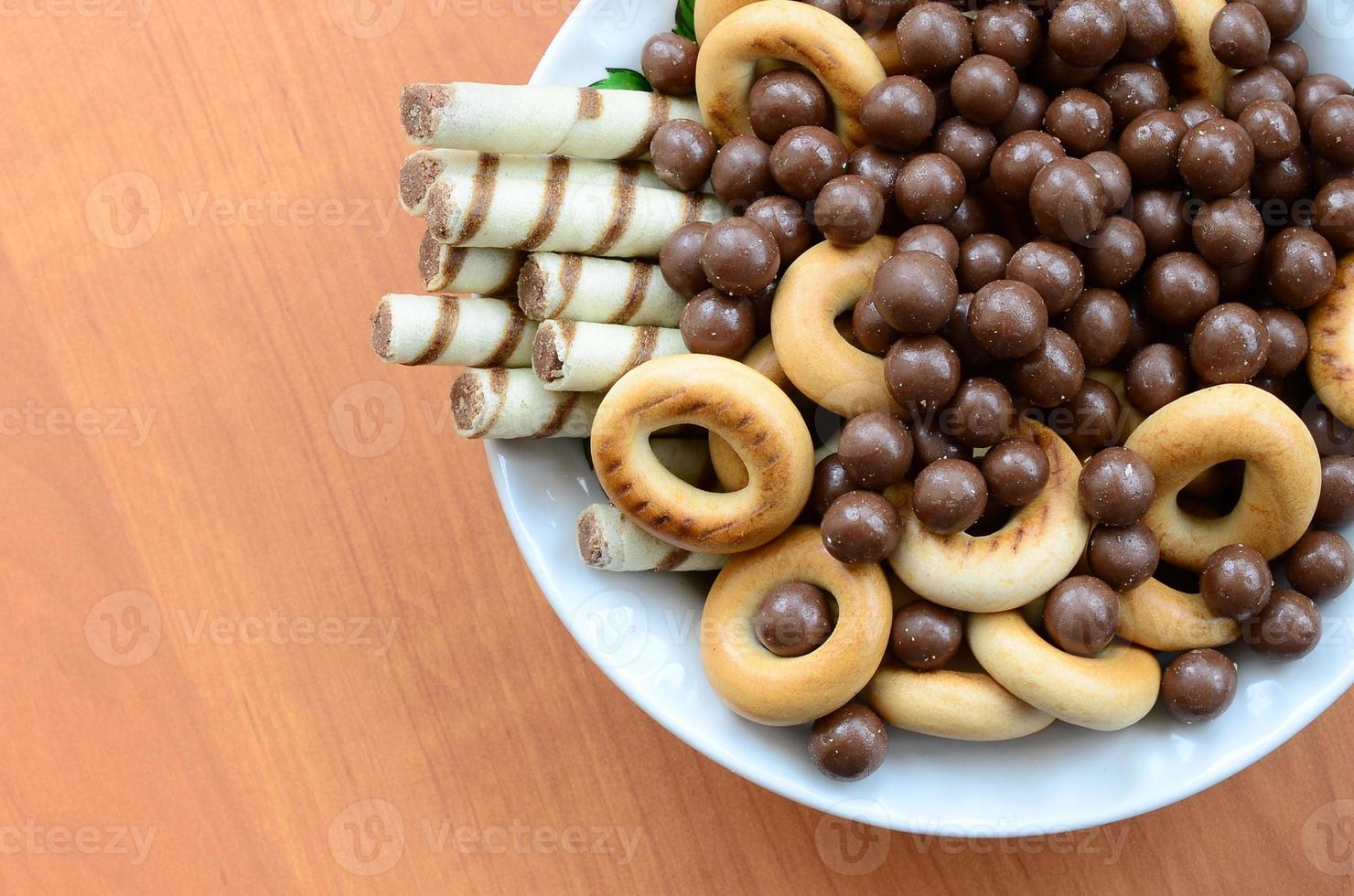 Crispy tubules, chocolate melting balls and bagels lie in a white plate on a wooden table. Mix of various sweets photo
