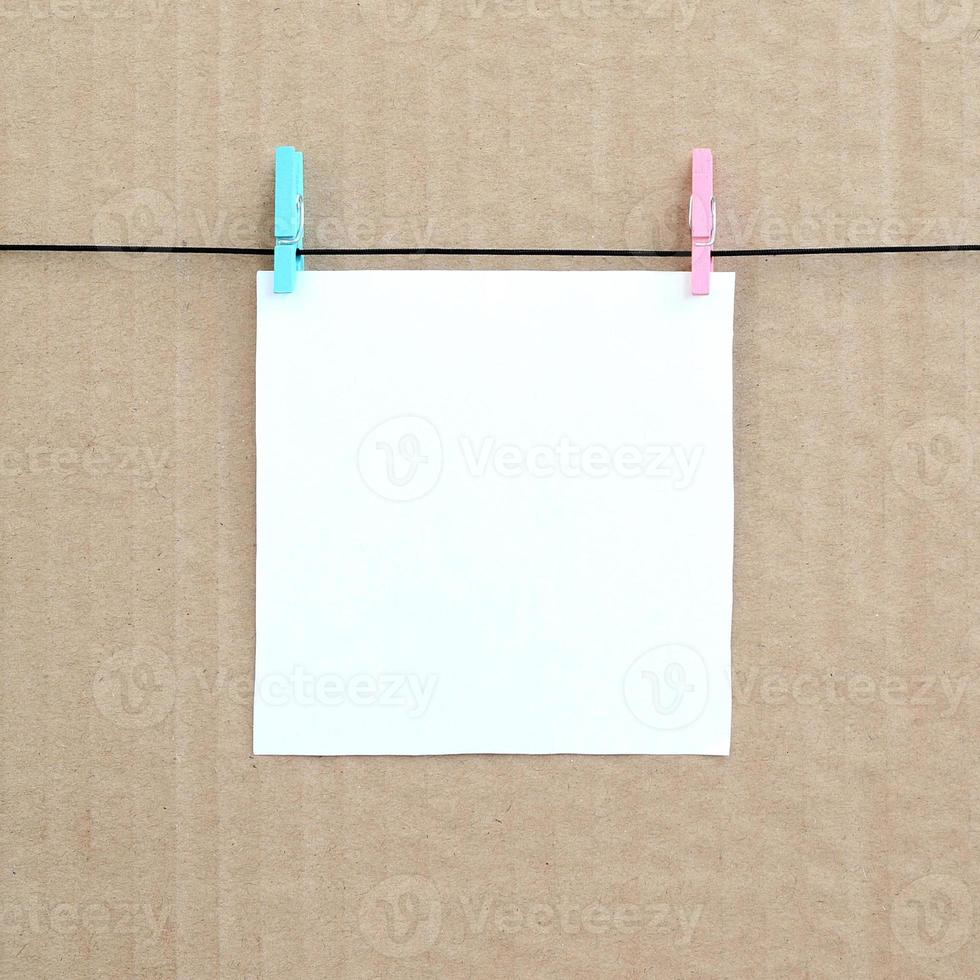 White blank card on rope on a brown cardboard background. Creative reminder, small sheet of paper on wooden clothespin, memo backdrop photo