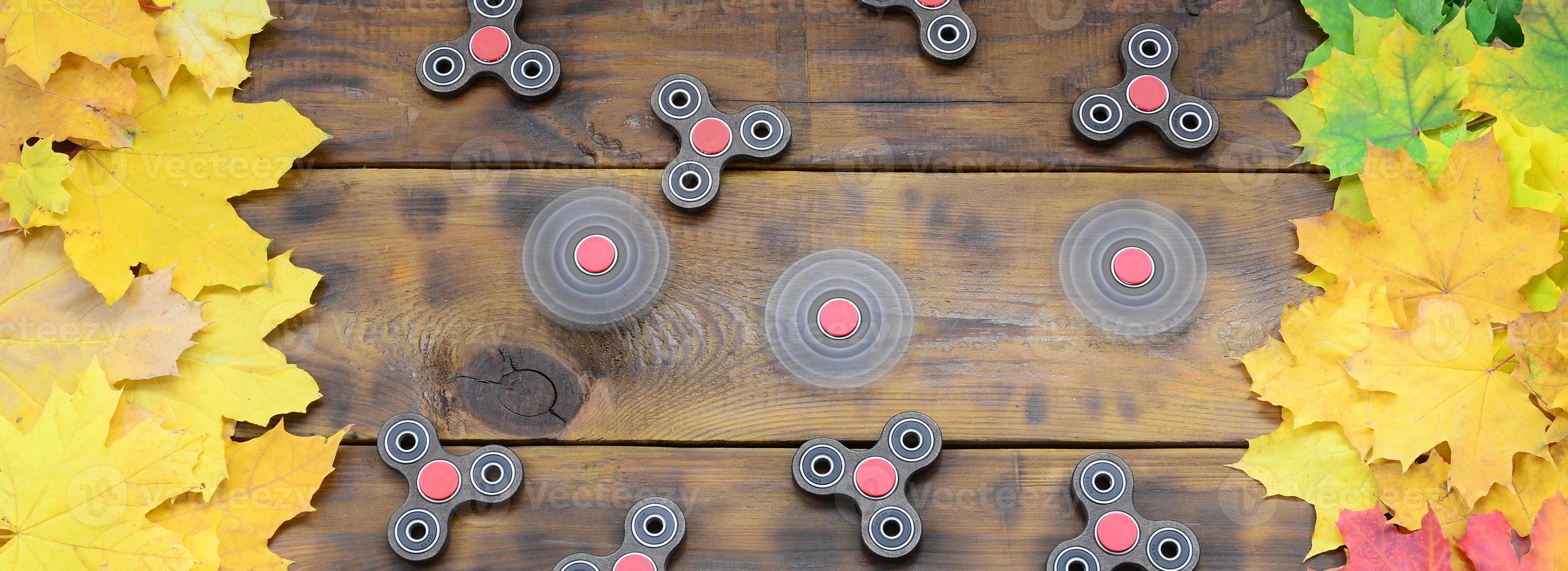 Several spinners among the many yellowing fallen autumn leaves on the background surface of natural wooden boards of dark brown color photo