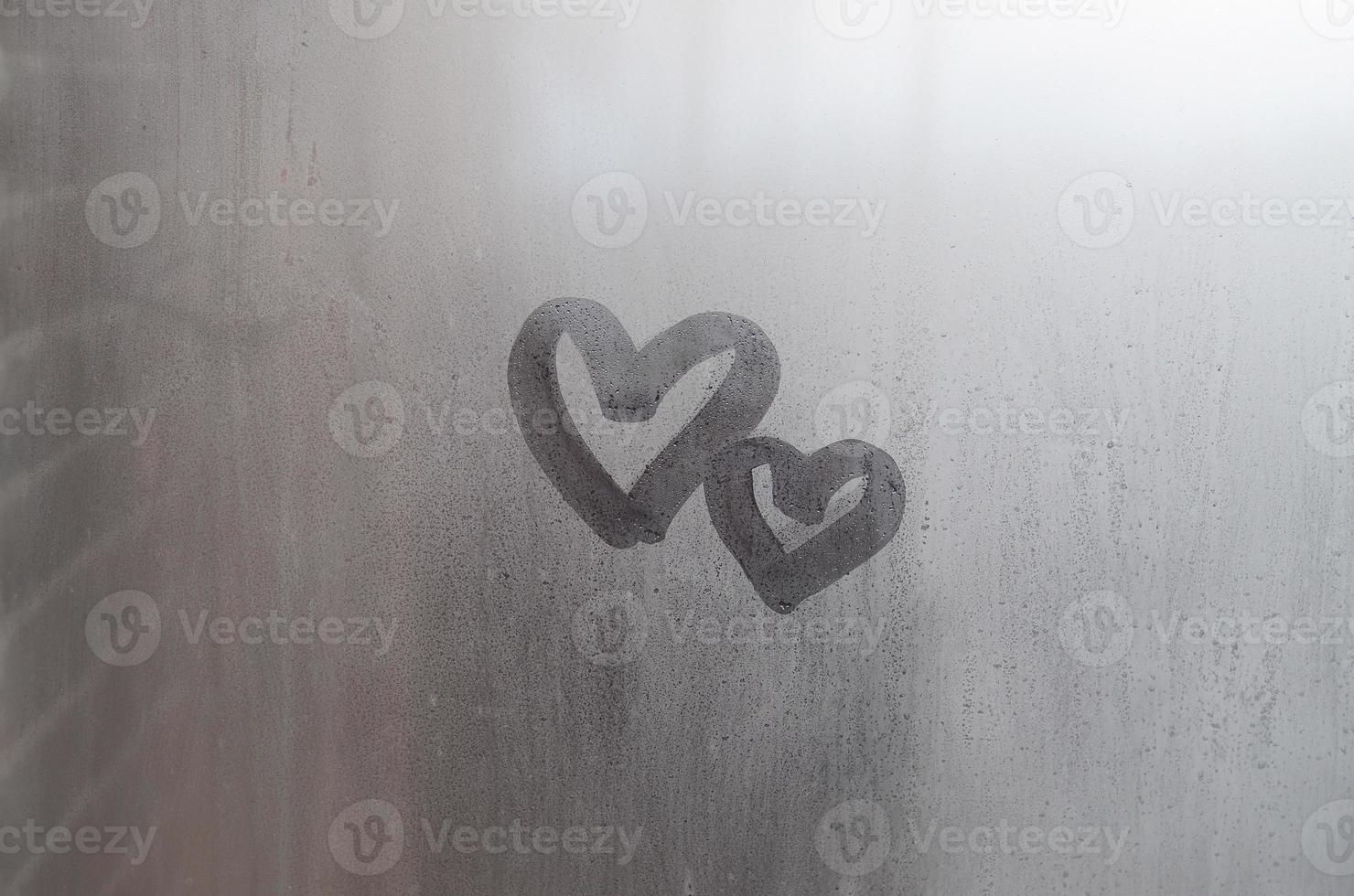 un par de símbolos de corazón de amor borrosos abstractos dibujados a mano en el cristal húmedo de la ventana con fondo de luz solar. plantilla para tarjetas postales del día de san valentín foto