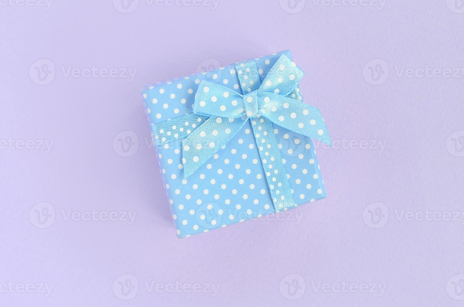 Small blue gift box with ribbon lies on a violet background. Minimalism flat lay top view photo