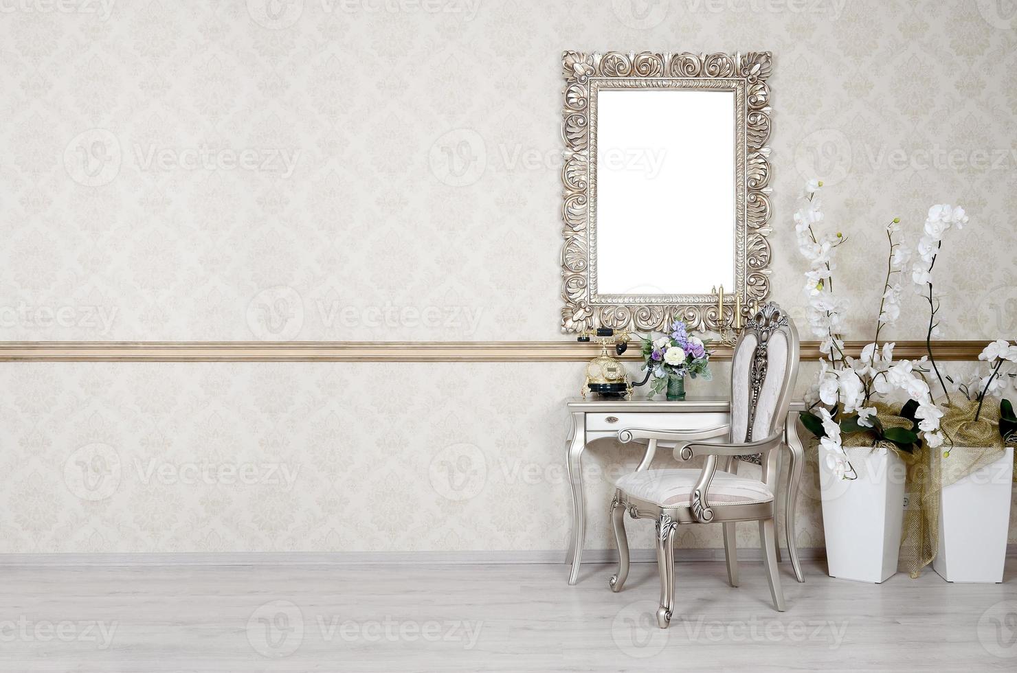 A fragment of a retro interior with a chair and table, on which is a telephone and a vase of flowers. Above the table hangs an empty picture frame for your photo