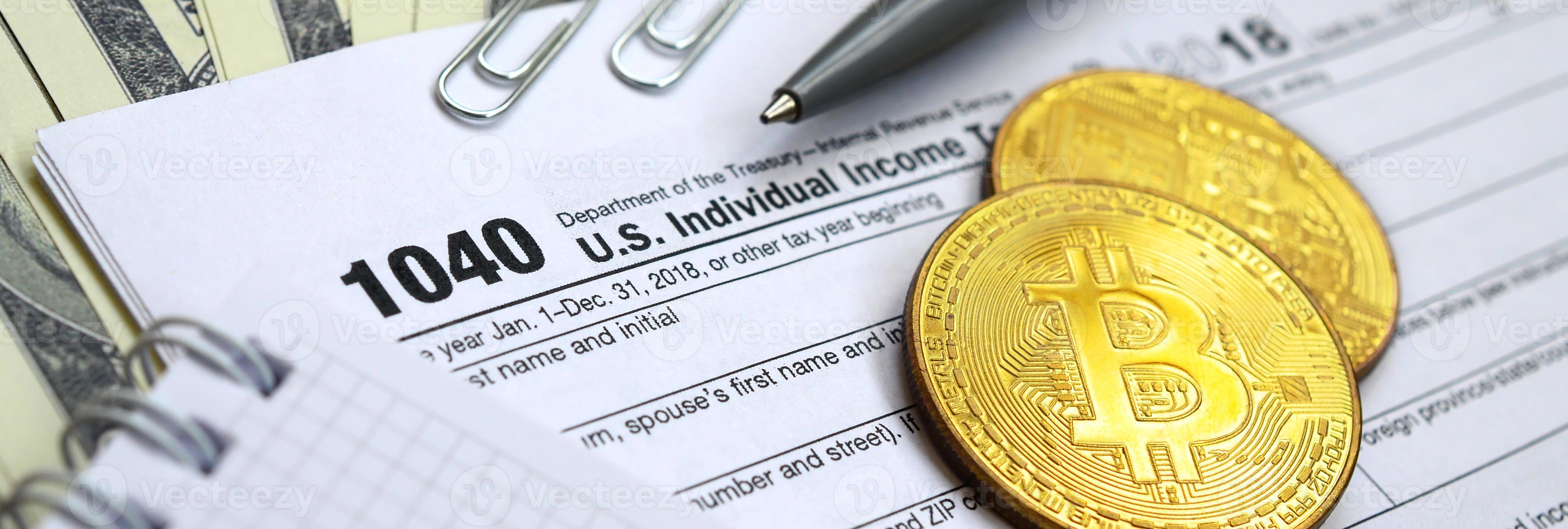 The pen, bitcoins and dollar bills is lies on the tax form 1040 U.S