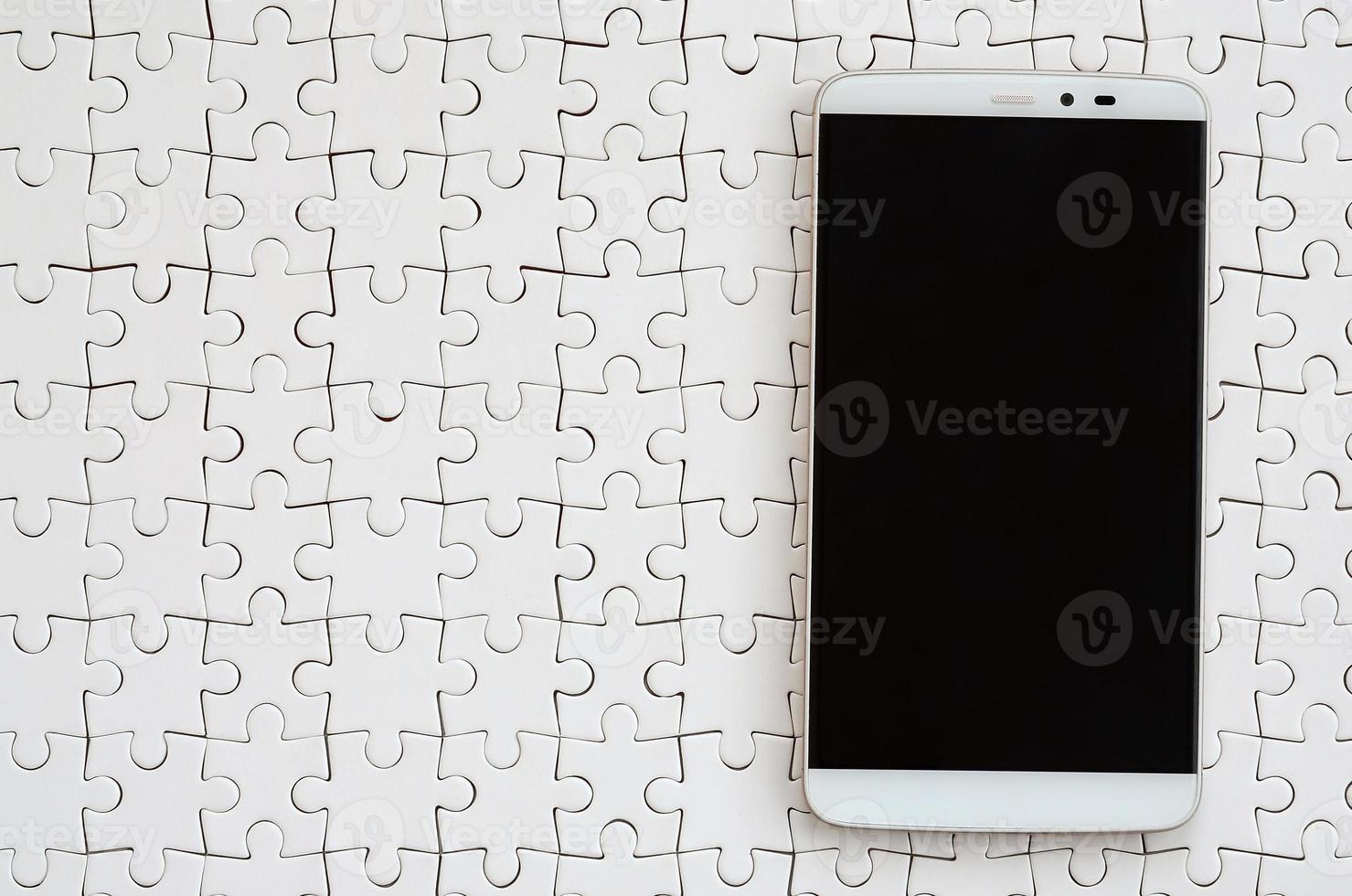 A modern big smartphone with a touch screen lies on a white jigsaw puzzle in an assembled state photo