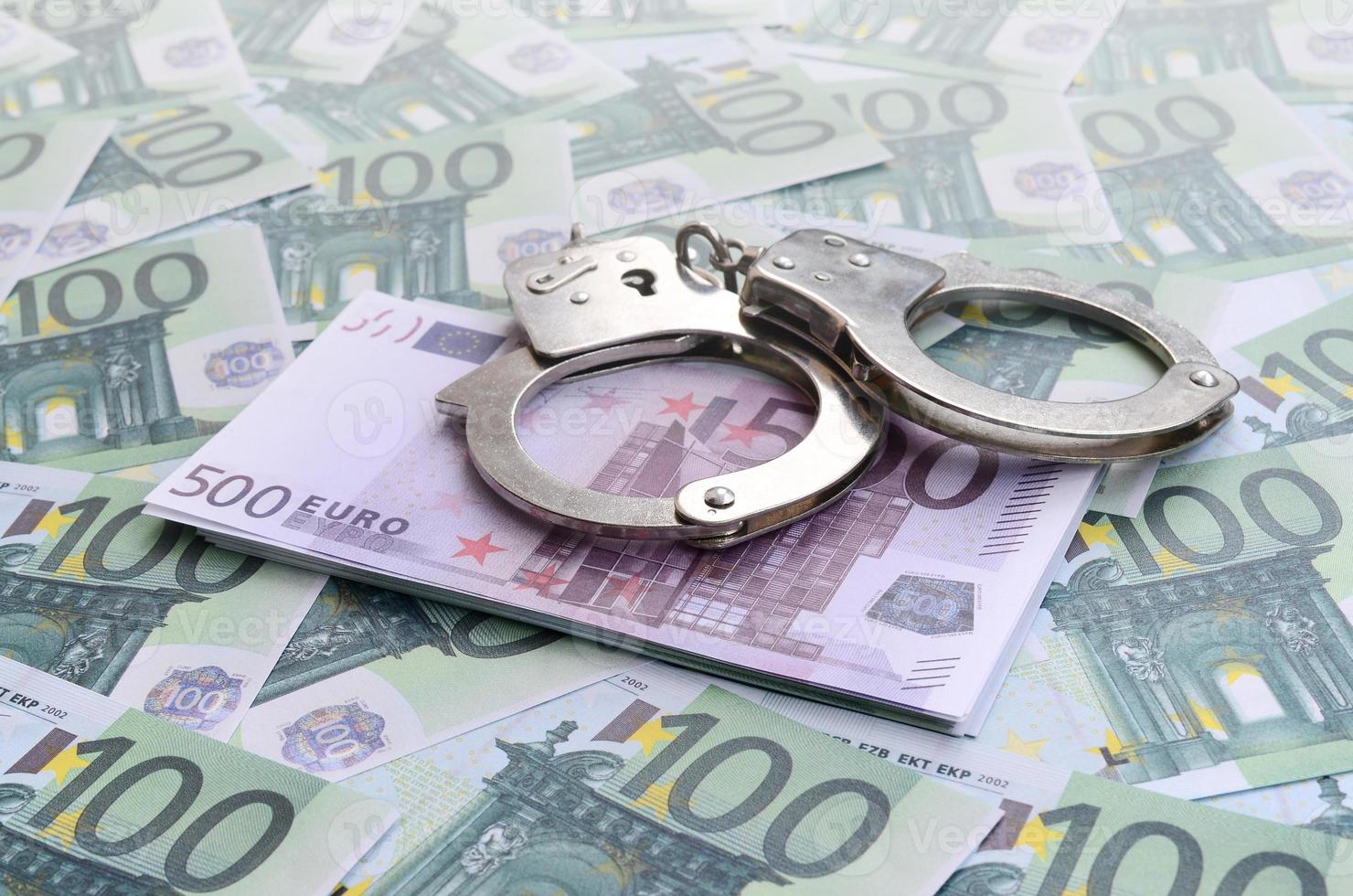 Police handcuffs lies on a set of green monetary denominations of 100 euros. A lot of money forms an infinite heap photo