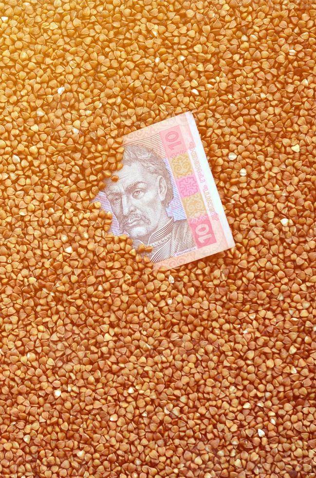 Background texture of a large pile of buckwheat, among which one can see a bill of one Ukrainian hryvnia. The concept of increasing prices for cereals in Ukraine photo