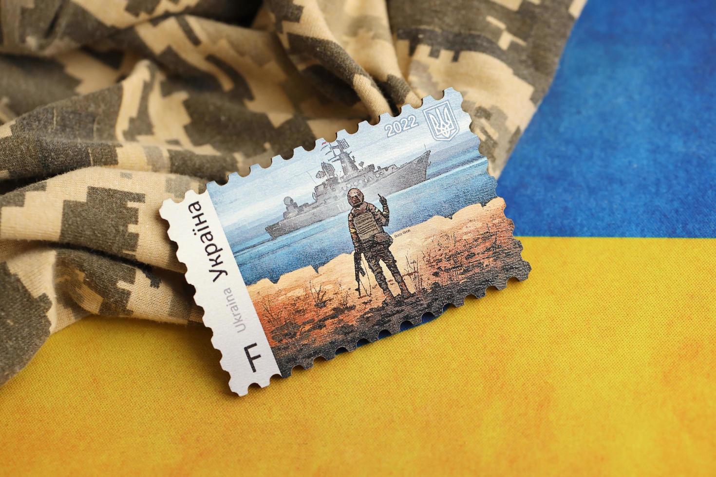 TERNOPIL, UKRAINE - SEPTEMBER 2, 2022 Famous Ukrainian postmark with russian warship and ukrainian soldier as wooden souvenir on army camouflage uniform and national flag photo