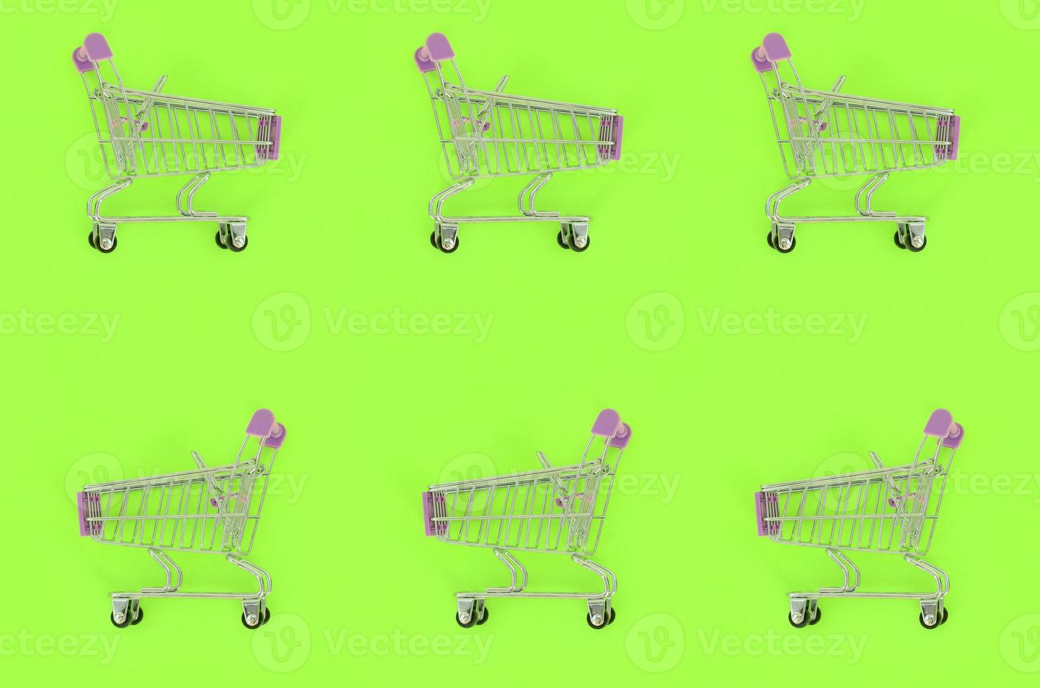 Shopping addiction, shopping lover or shopaholic concept. Many small empty shopping carts perform a pattern on a pastel colored paper background. Flat lay composition, top view photo