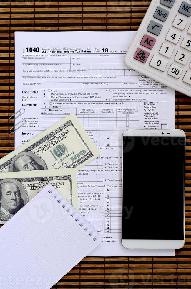 Composition of items lying on the 1040 tax form. Dollar bills, calculator, smartphone, paper clip and notepad. The time to pay taxes photo