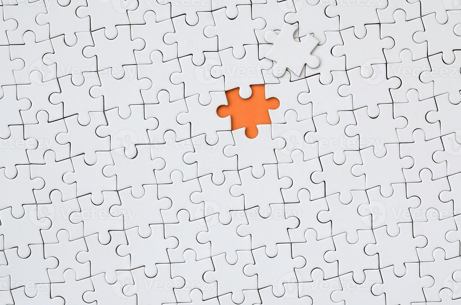 The texture of a white jigsaw puzzle in an assembled state with one missing element forming an orange space photo