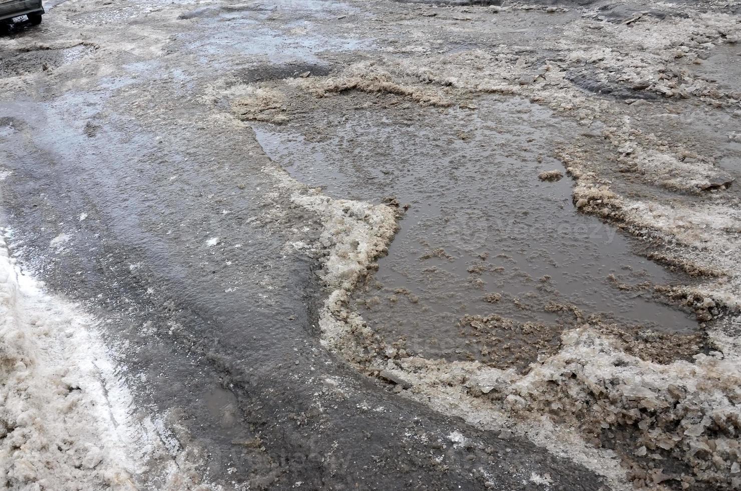 Damaged asphalt road with potholes caused by freezing and thawing cycles during the winter. Poor road photo