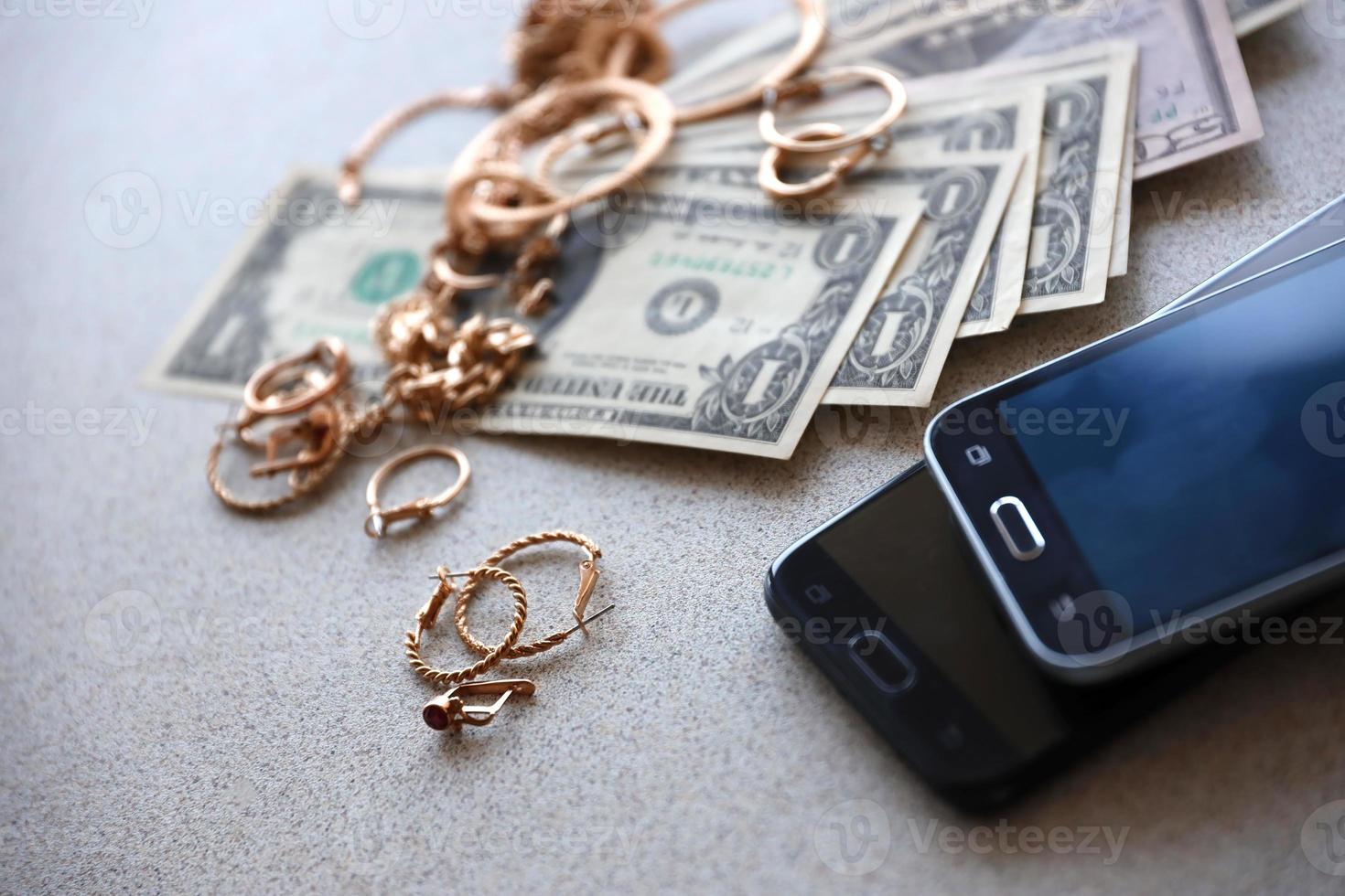 Many expensive golden jewerly rings, earrings and necklaces with big amount of US dollar bills close to smartphones. Pawn shop photo