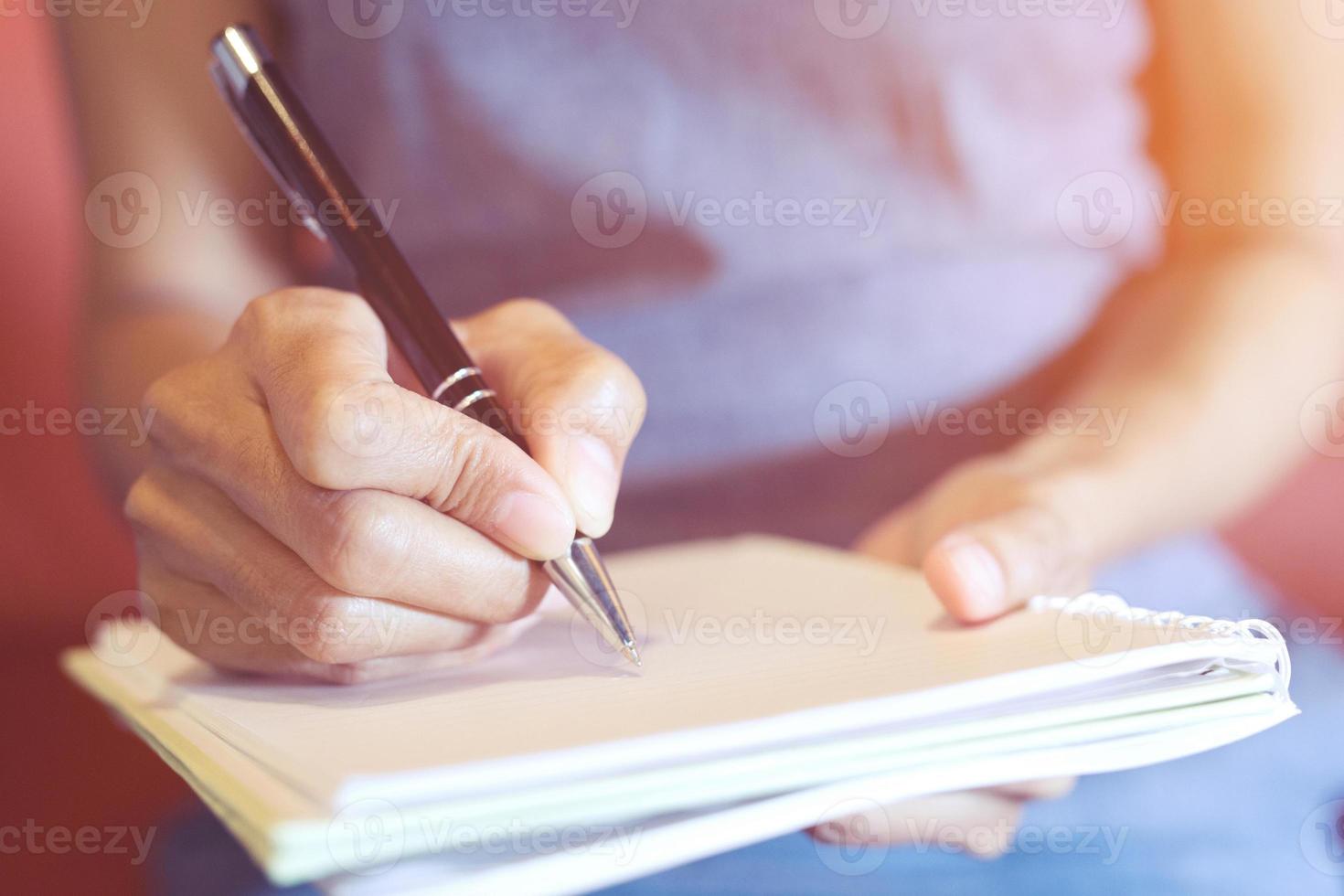close up hand young woman are sitting on a chair. using pen writing Record Lecture note pad into the book on the table. photo