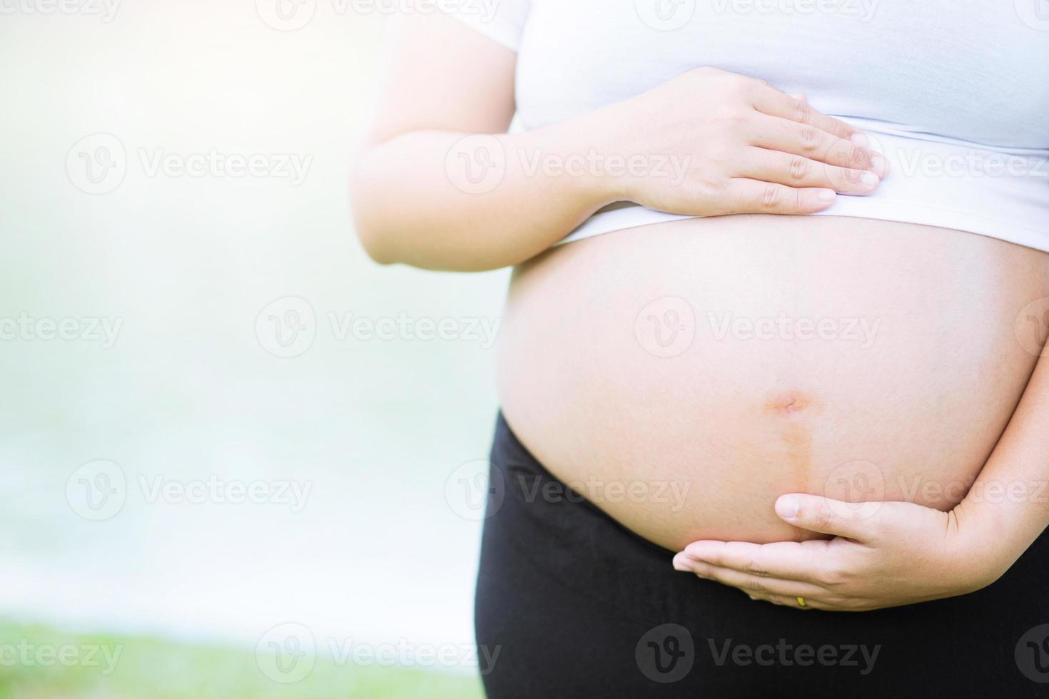 pregnant woman and her husband hand splice hugging the tummy Heart shaped show love for the unborn baby in the belly relaxing at home in bedroom. wait birth date expecting a baby stand in the outdoors photo