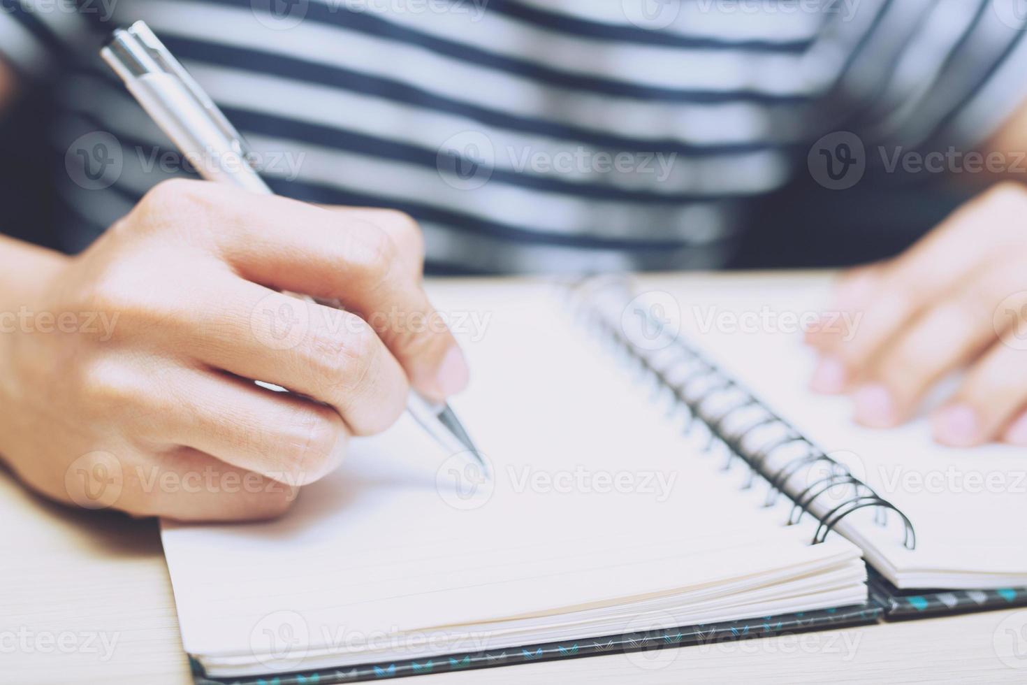 close up business woman hand holding in pen open the page notepad Office desk table with book, equipment supplies in the work spectacles and coffee cup. Top view with copy space on the page paper. photo