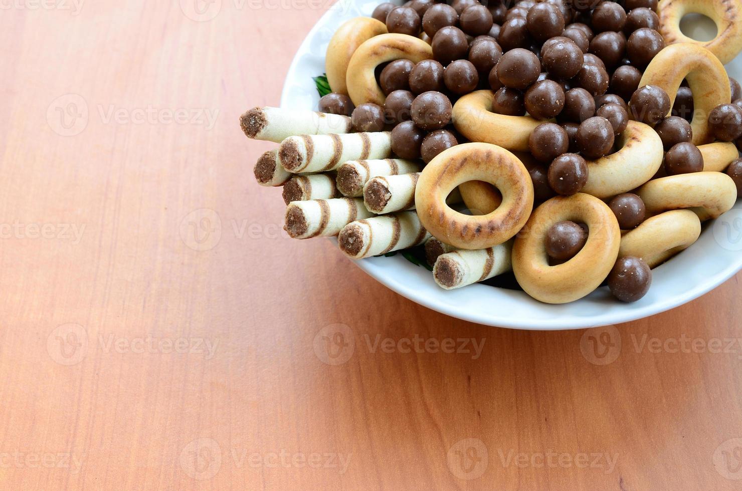 Crispy tubules, chocolate melting balls and bagels lie in a white plate on a wooden table. Mix of various sweets photo