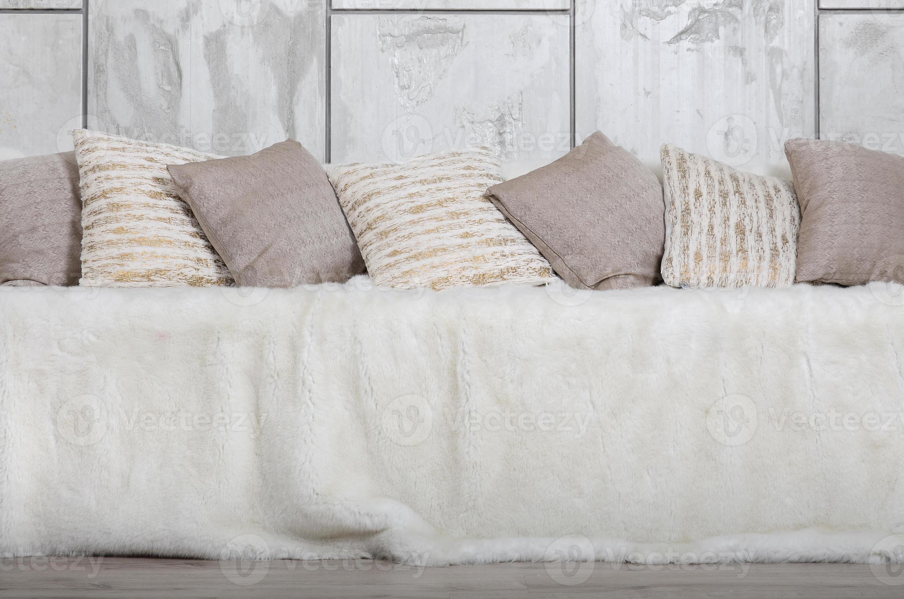 Many pillows lie on the couch, which is covered with a large plush veil against the background