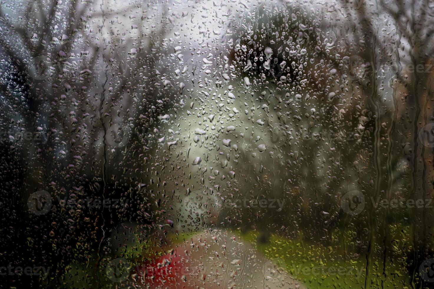 ventana lluviosa, gotas de lluvia otoñales en el vidrio contra el telón de fondo de una naturaleza aburrida con árboles y un sendero. foto