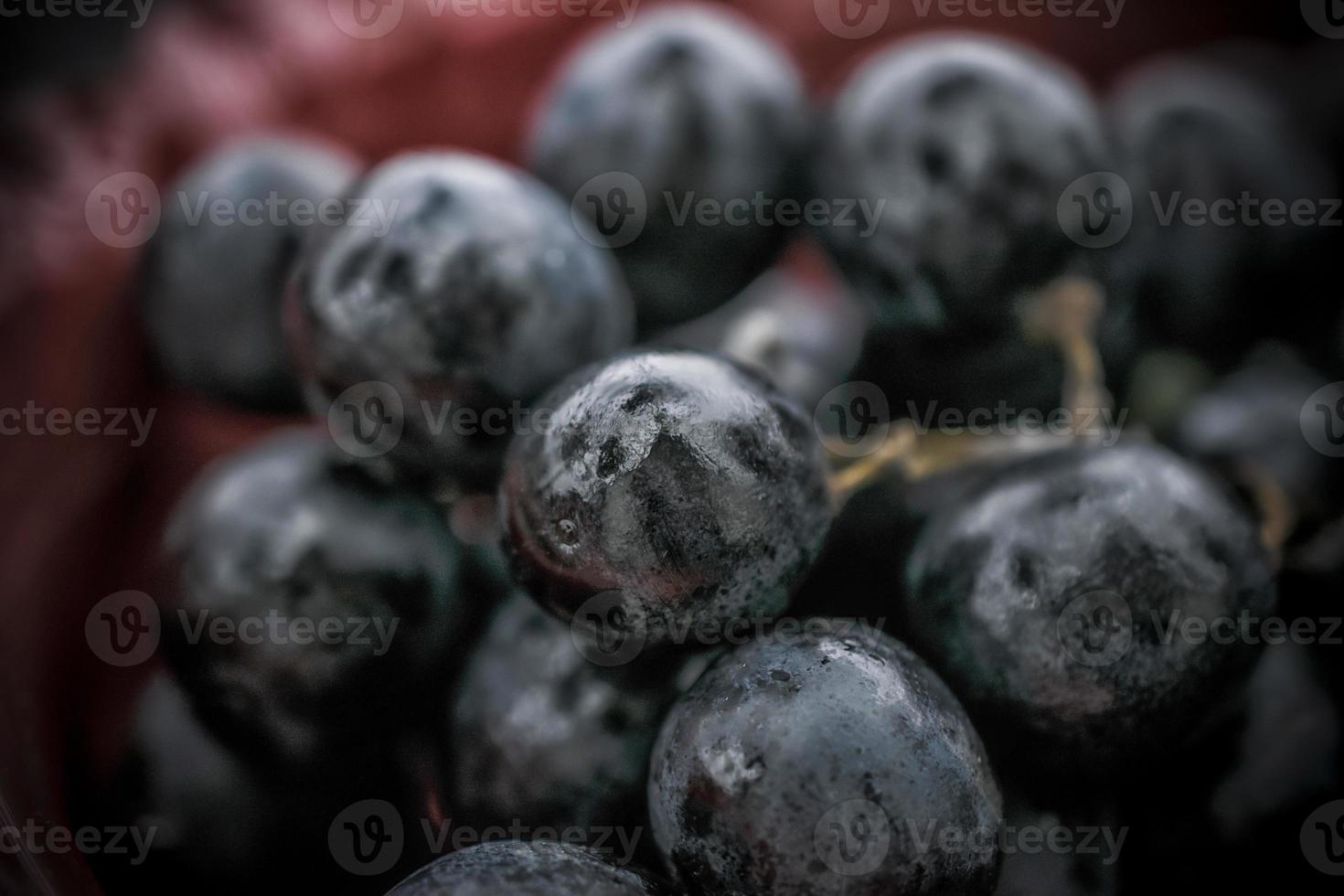 A close-up photo of black grapes in a red bowl