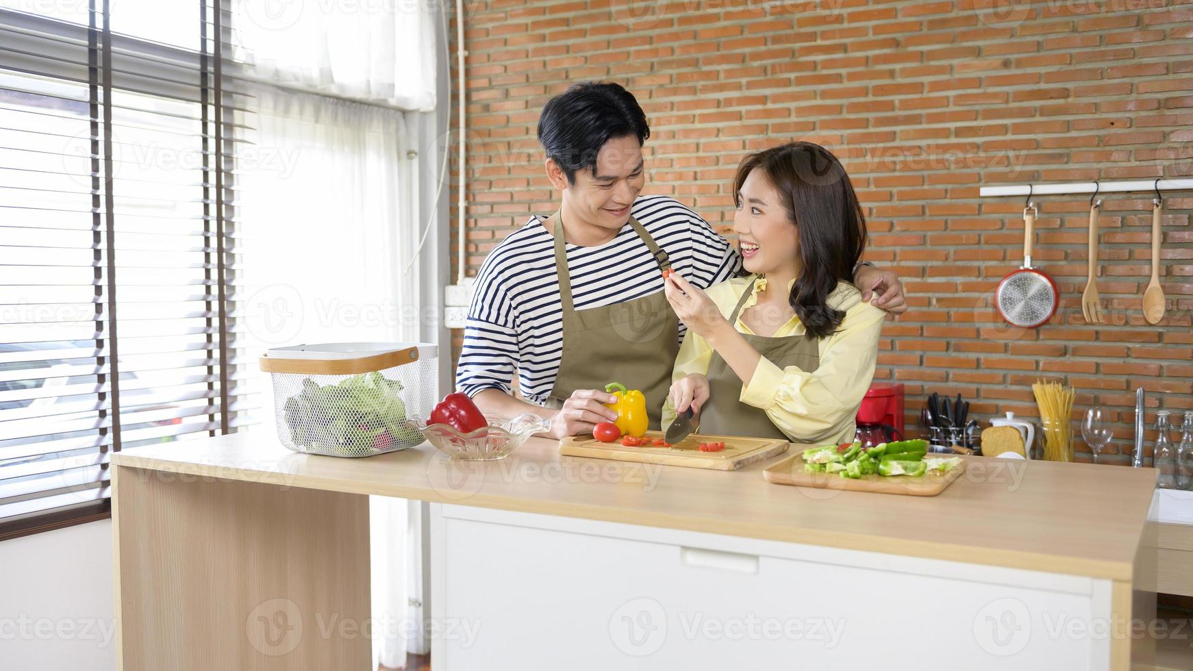 Young smiling asian couple wearing an apron in the kitchen room, cooking concept photo