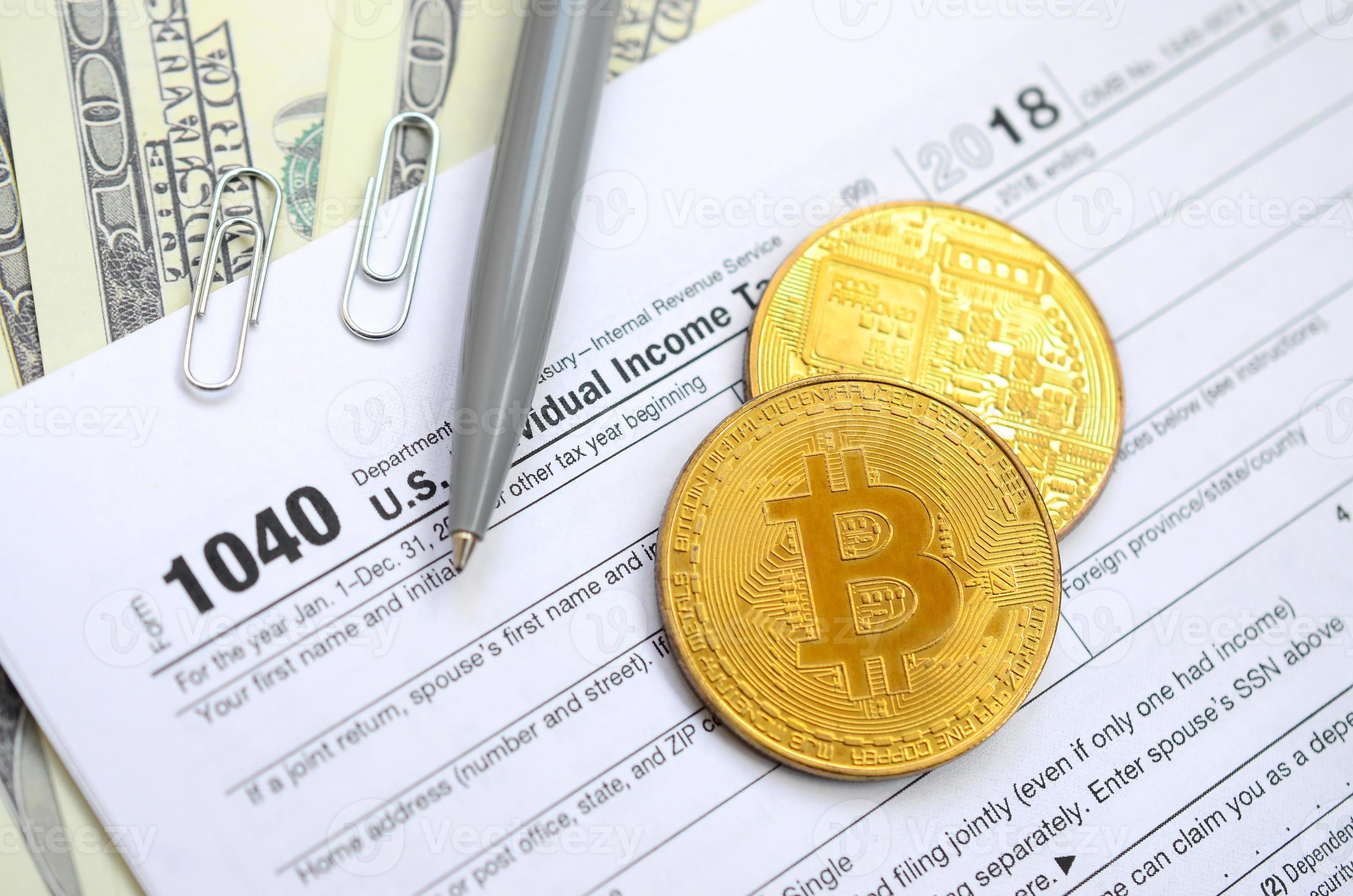 The pen, bitcoins and dollar bills is lies on the tax form 1040 U.S