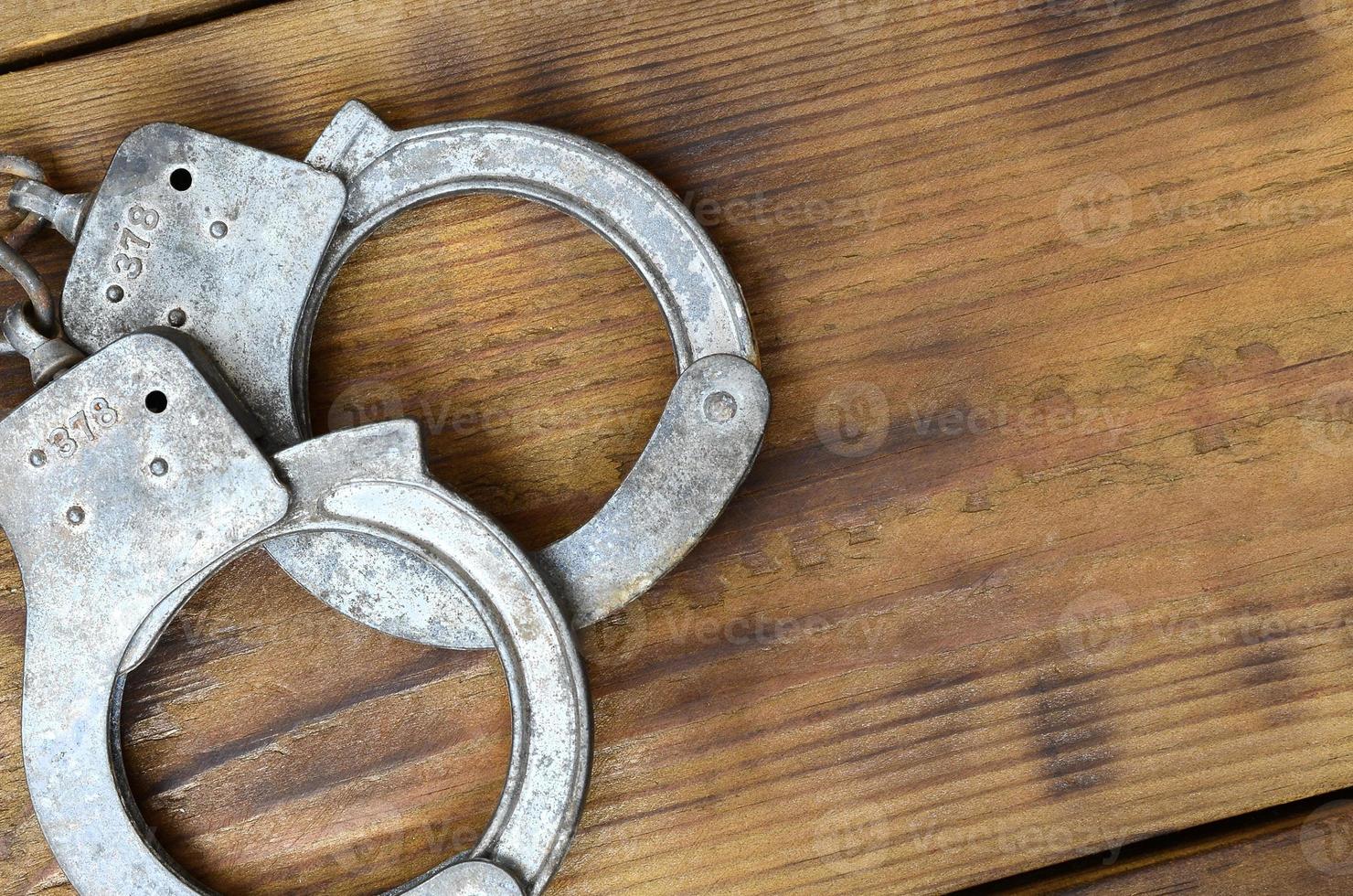 Old and rusty police handcuffs lie on a scratched wooden surface. The concept of an old crime photo