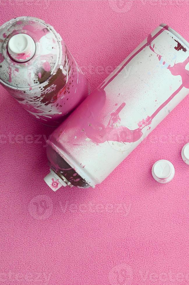 algunas latas de aerosol rosa usadas y boquillas con gotas de pintura se encuentran sobre una manta de suave y peluda tela de lana rosa claro. color de diseño femenino clásico. concepto de vandalismo de graffiti foto