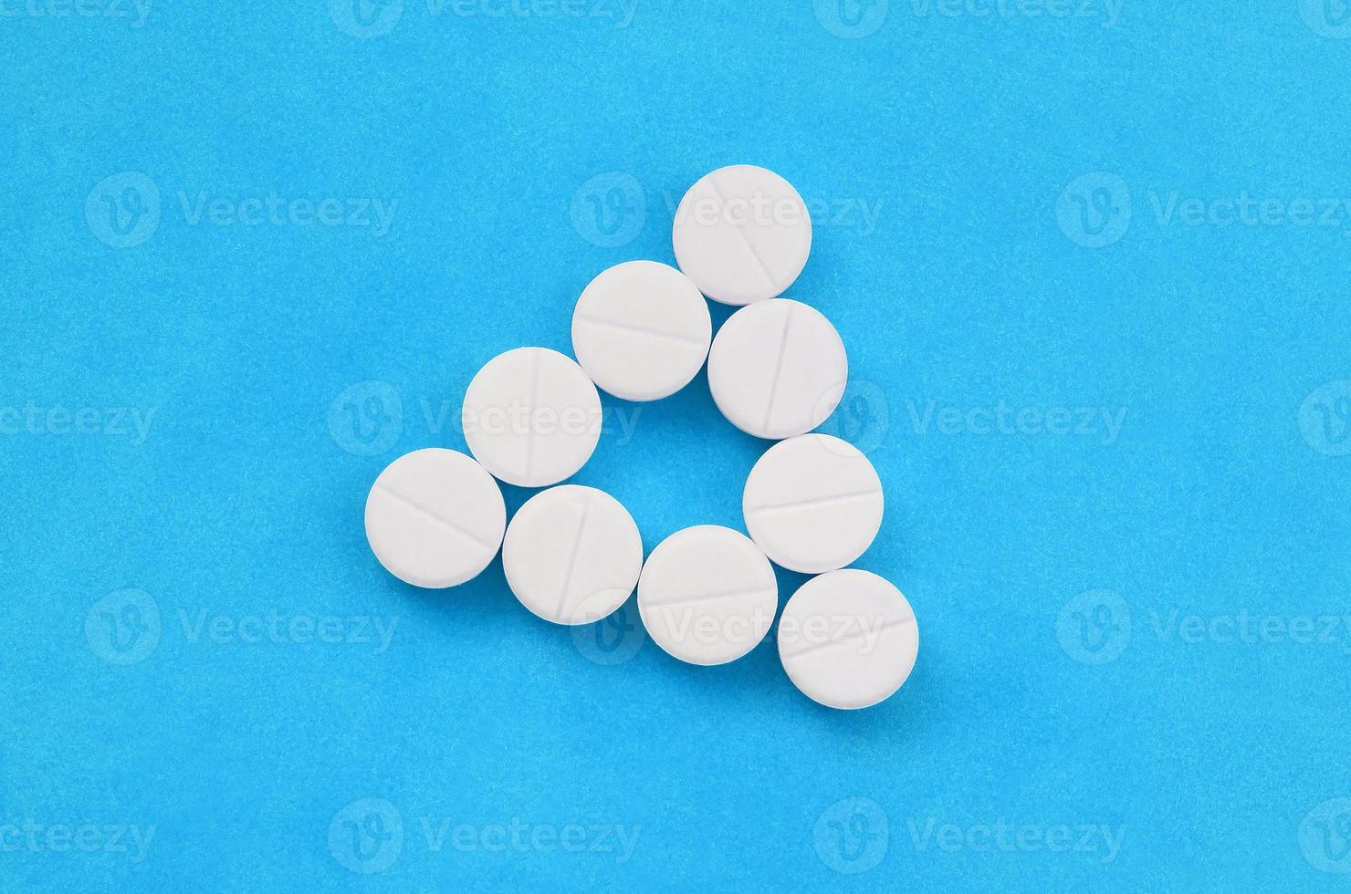 Several white tablets lie on a bright blue background in the form of an even triangle. Background image on medicine and pharmaceutical topics photo