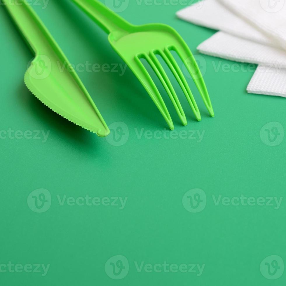 Disposable plastic cutlery green. Plastic fork and knife lie on a green background surface next to napkins photo