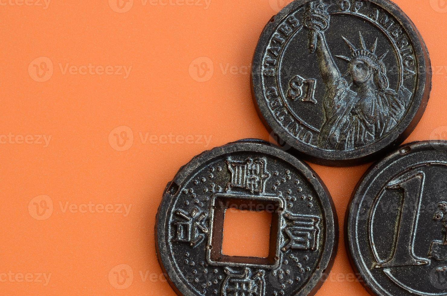 Three chocolate products in the form of Euro, USA and Japan coins lie on an orange plastic background. A model of cash coins in an edible form photo