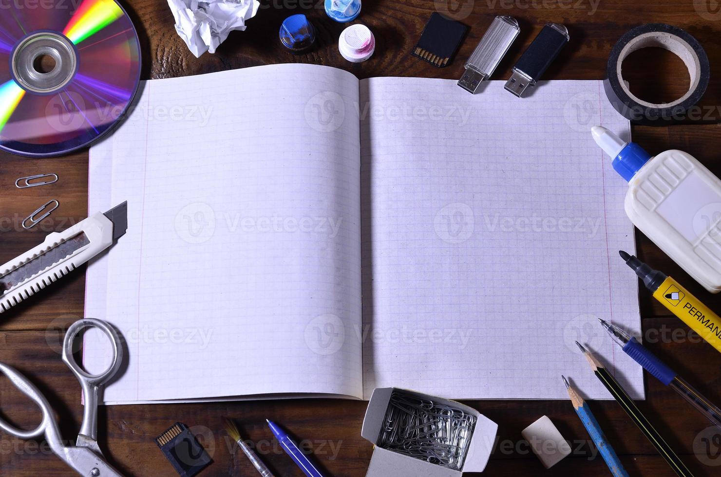 un bodegón escolar o de oficina con un cuaderno escolar abierto o chequera y muchos suministros de oficina. los útiles escolares se encuentran sobre un fondo de madera marrón. lugar para texto foto