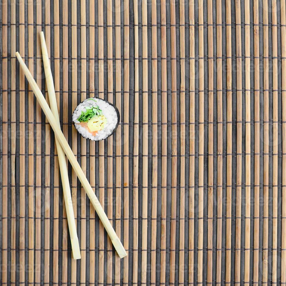 Sushi roll and wooden chopsticks lie on a bamboo straw serwing mat. Traditional Asian food. Top view. Flat lay minimalism shot with copy space photo